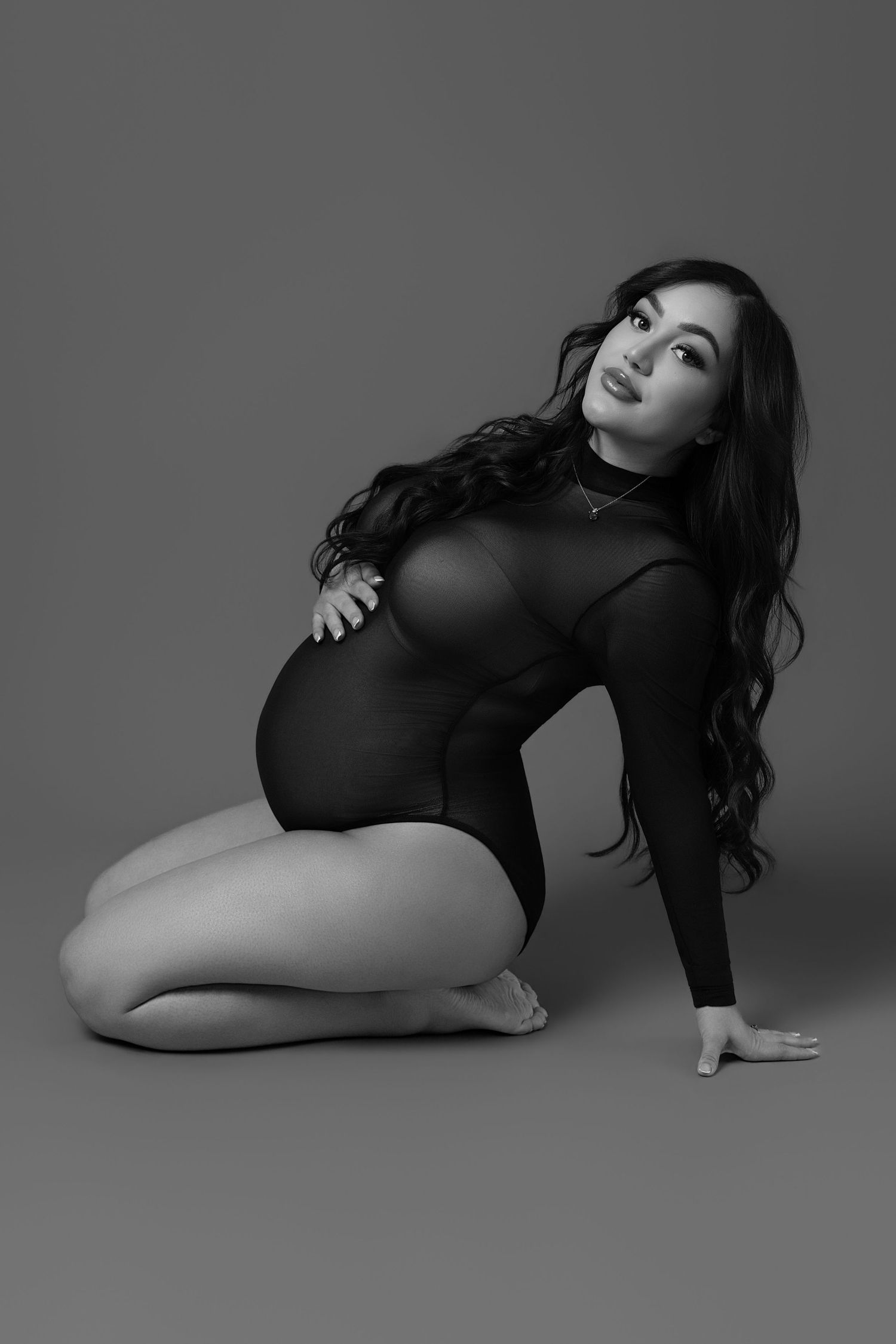 Artistic black and white fashion photo series showing model in bodysuit posing on floor in dramatic lighting.