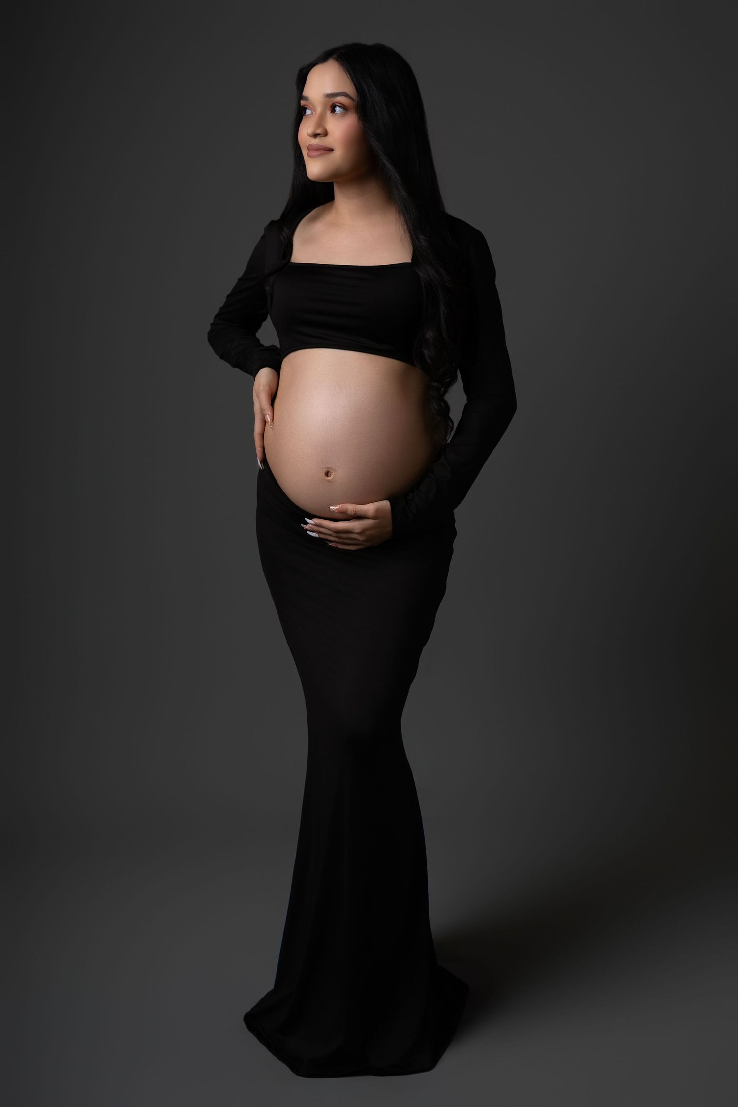 Artistic maternity photo series in black dress against dark background showing silhouette and bare pregnant belly.