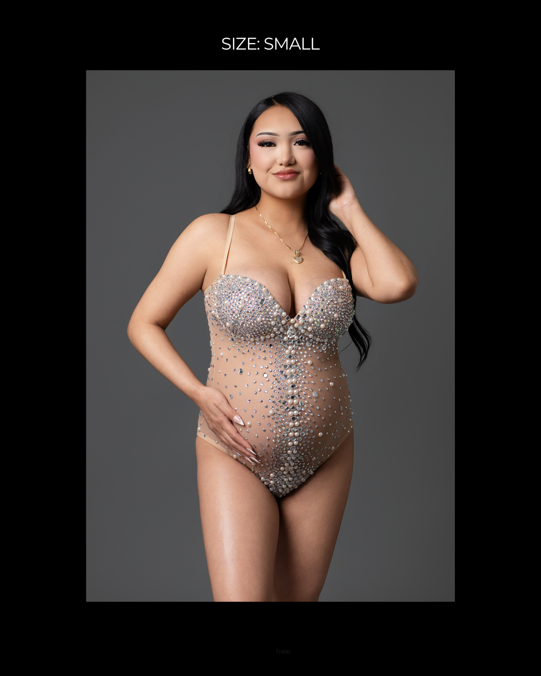Pregnant woman in a small size crystal-embellished nude maternity bodysuit, posing elegantly in a studio setting.
