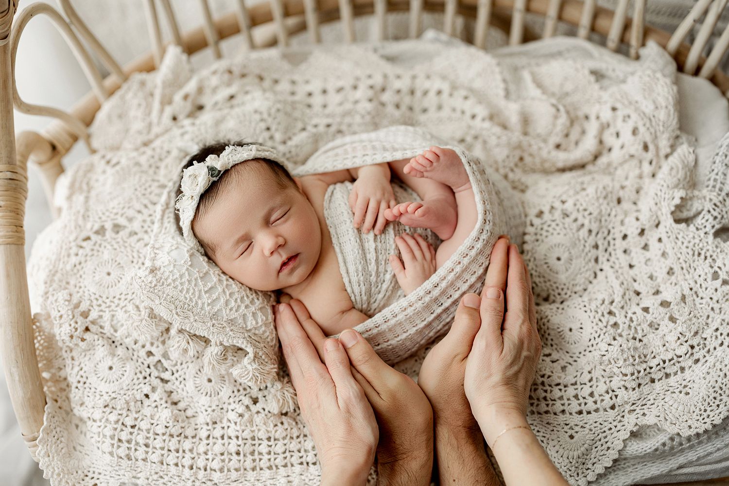 Sweet newborn baby curled up on soft white lace blanket in gentle lighting setup.