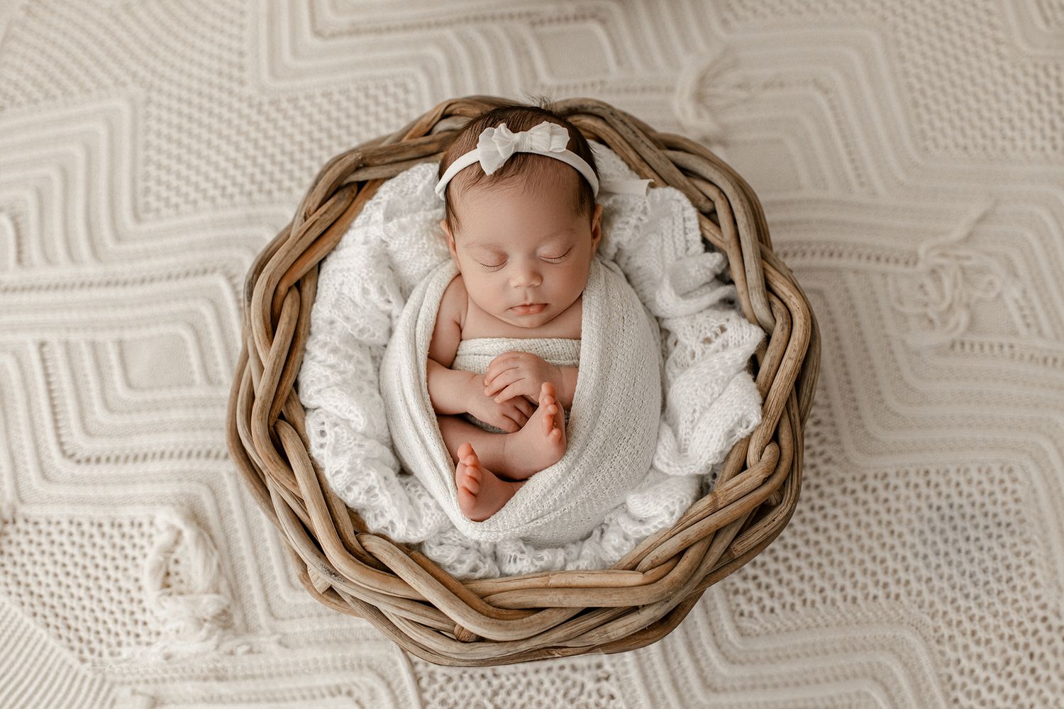 A sleeping newborn baby nestled in a round woven basket on textured white bedding.