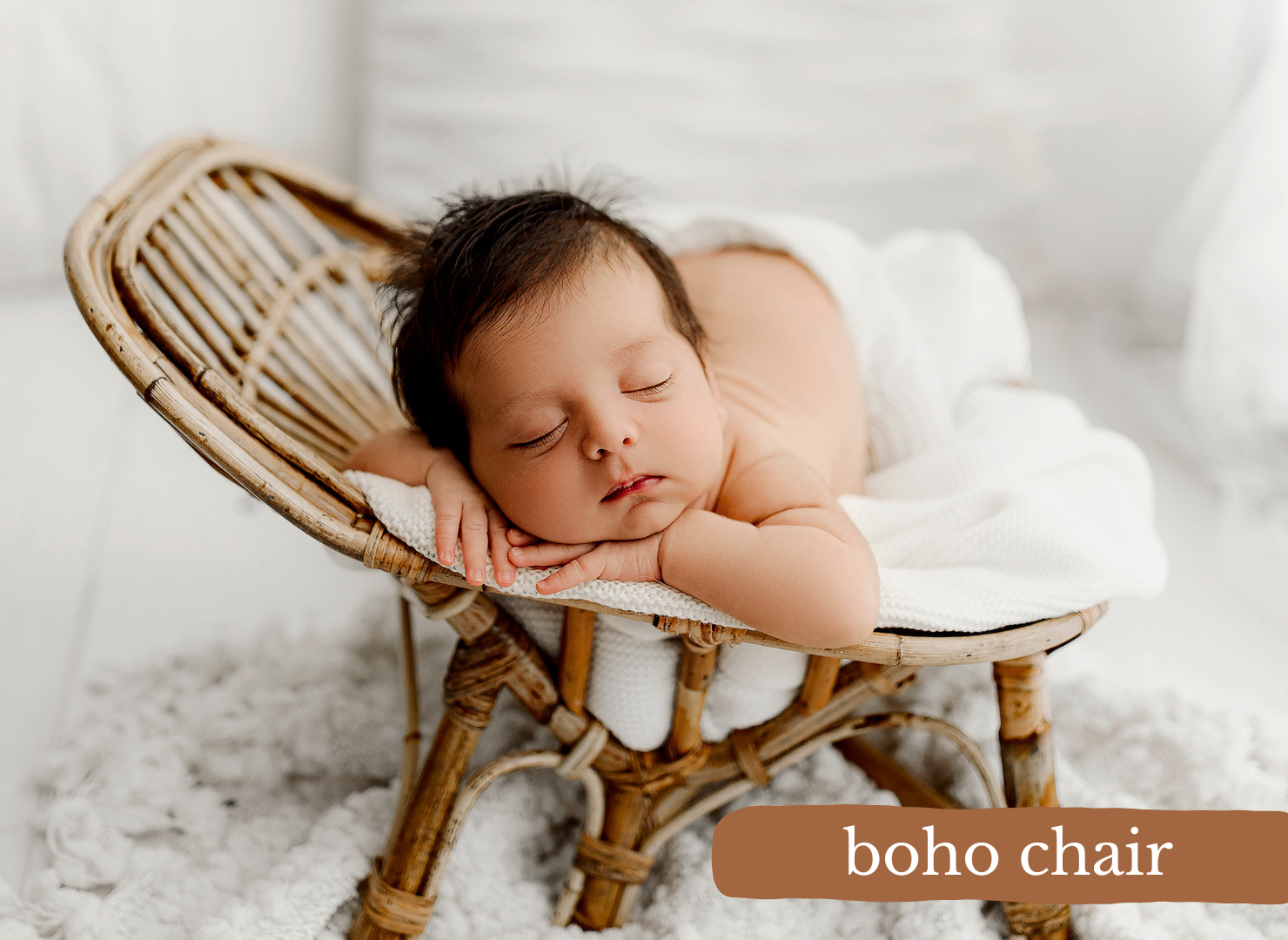 Newborn baby sleeping peacefully in a small boho rattan chair on a white fluffy rug.