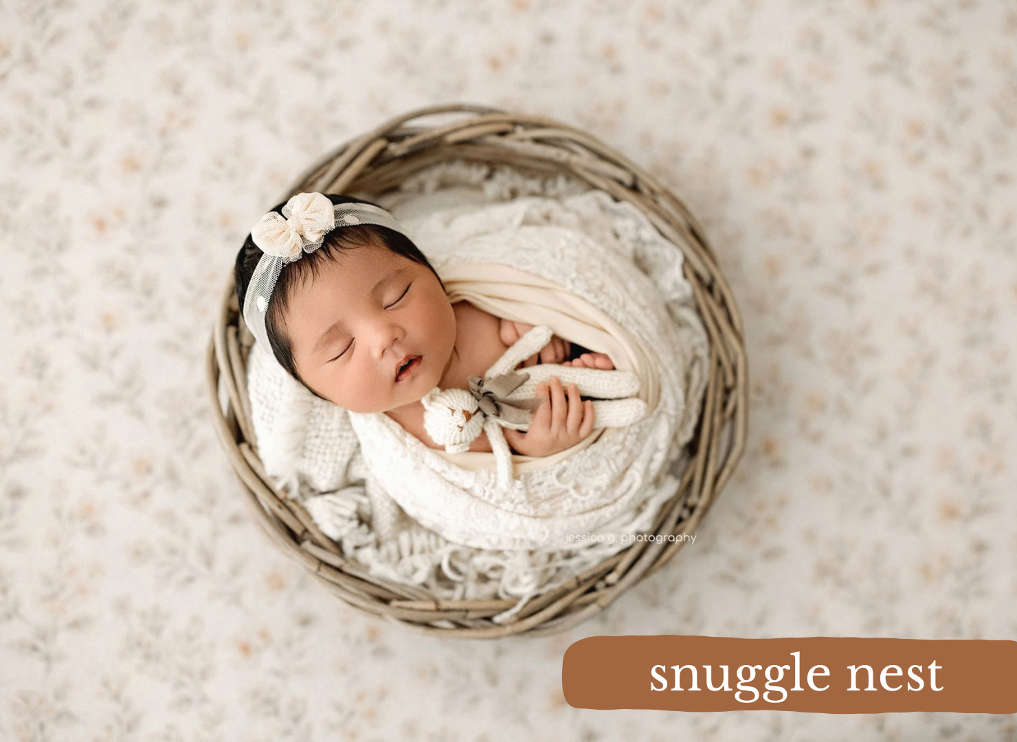 Newborn baby sleeping peacefully in a wicker nest bowl with cream wrap and floral headband, labeled snuggle nest.
