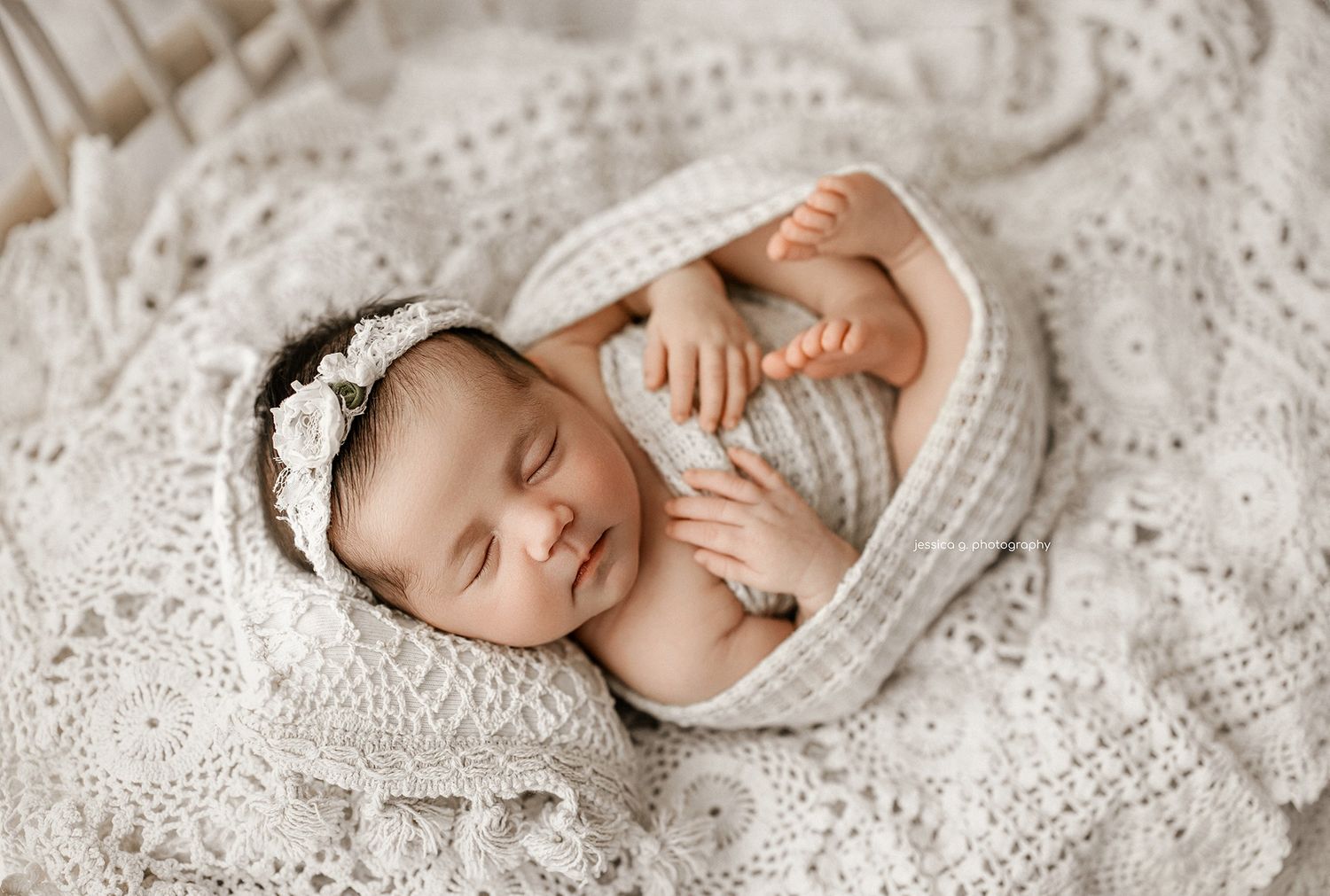 A sleeping newborn baby lies on white lace fabric in a dreamy and serene pose during a professional photo session.