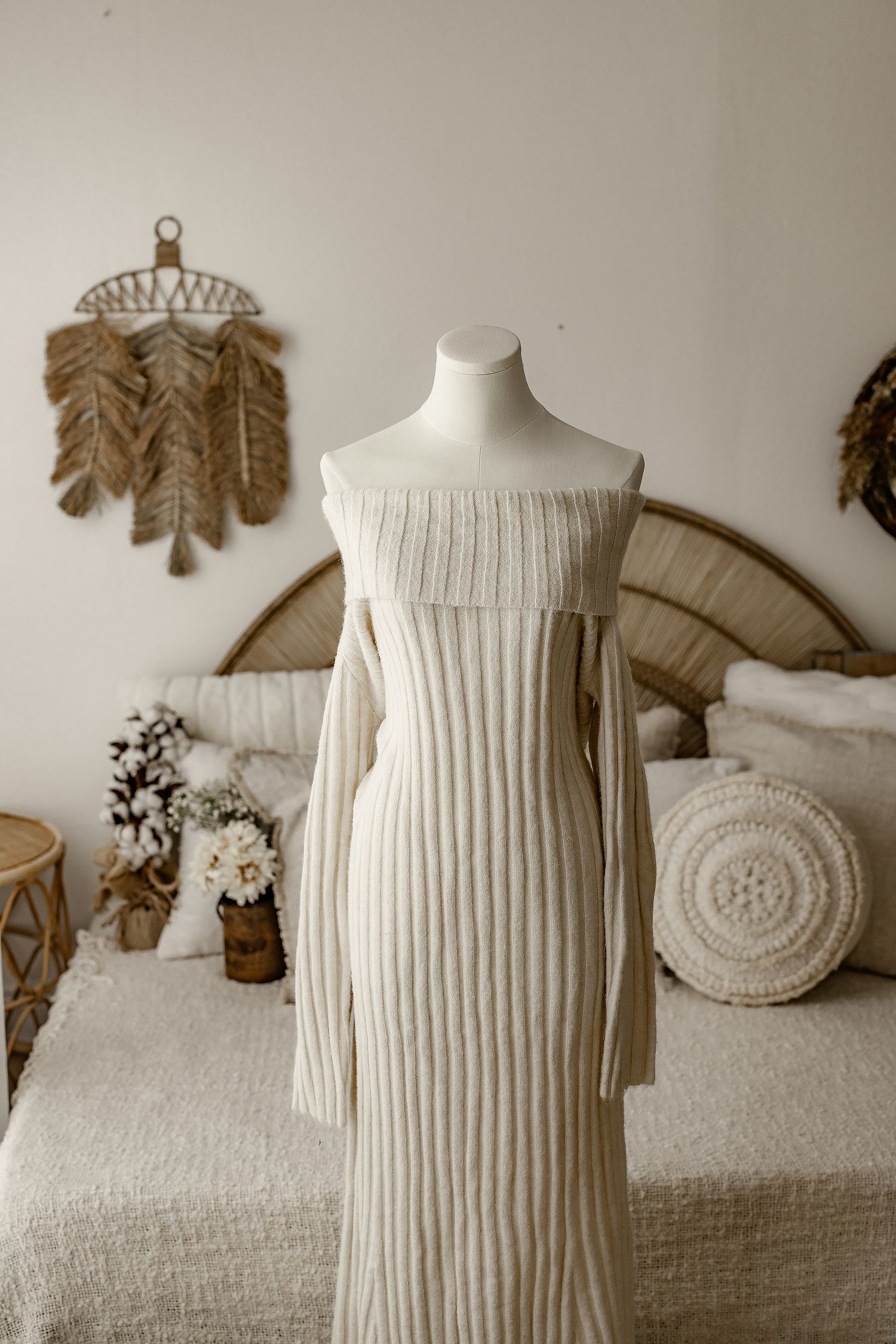 Ribbed off-shoulder cream maternity dress on mannequin with boho wall decor background.