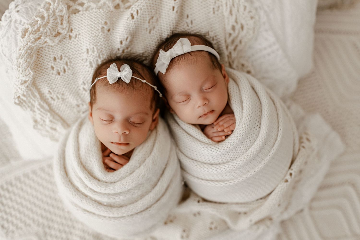 A series of sleeping newborns swaddled in white blankets arranged in a collage style layout.