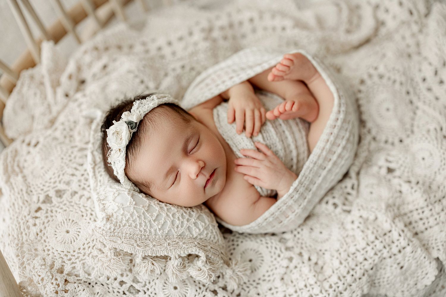 Newborn baby sleeping peacefully on white lace blanket in natural light studio setting.