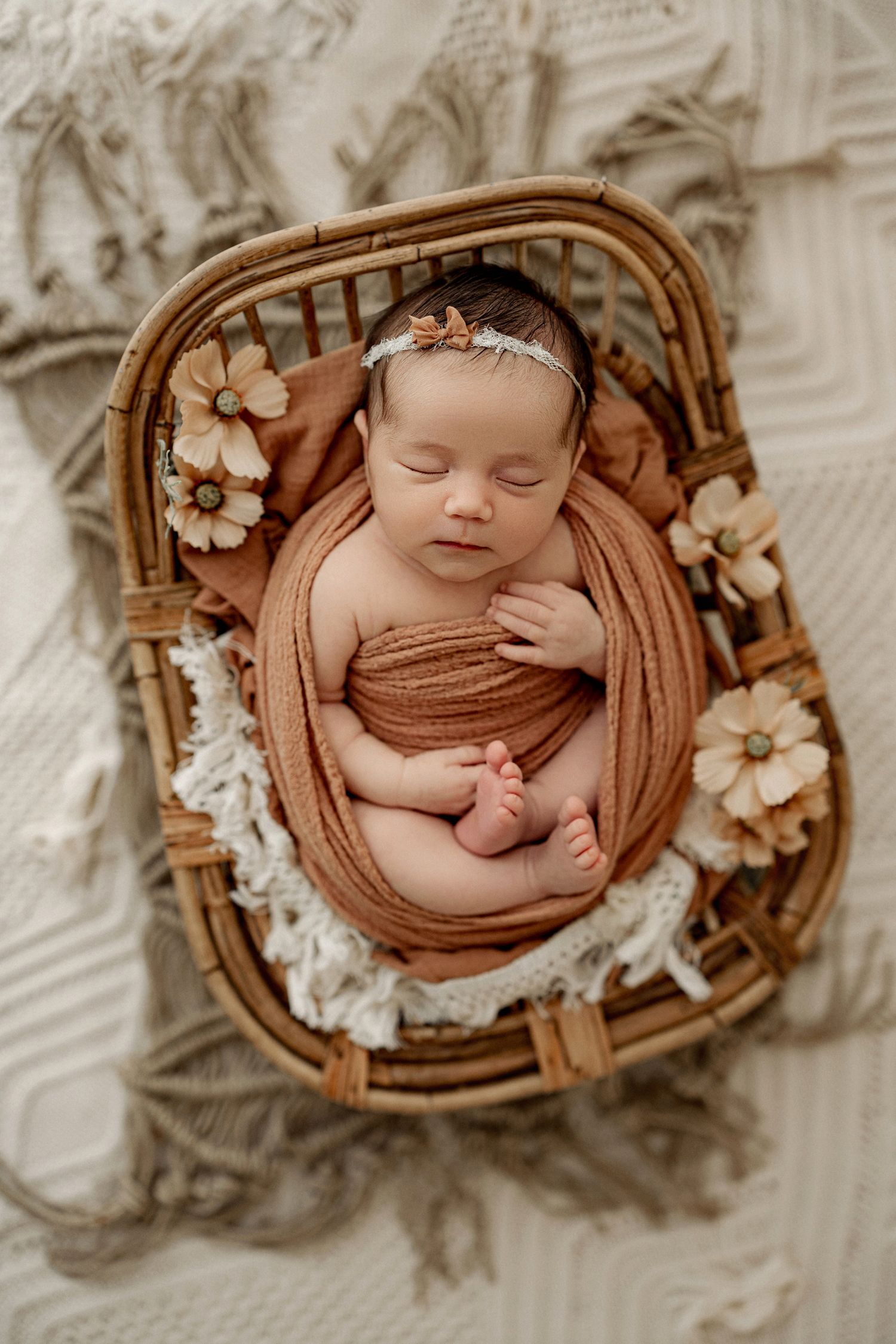 Sleeping newborn in neutral brown basket with delicate floral accents in five similar poses.