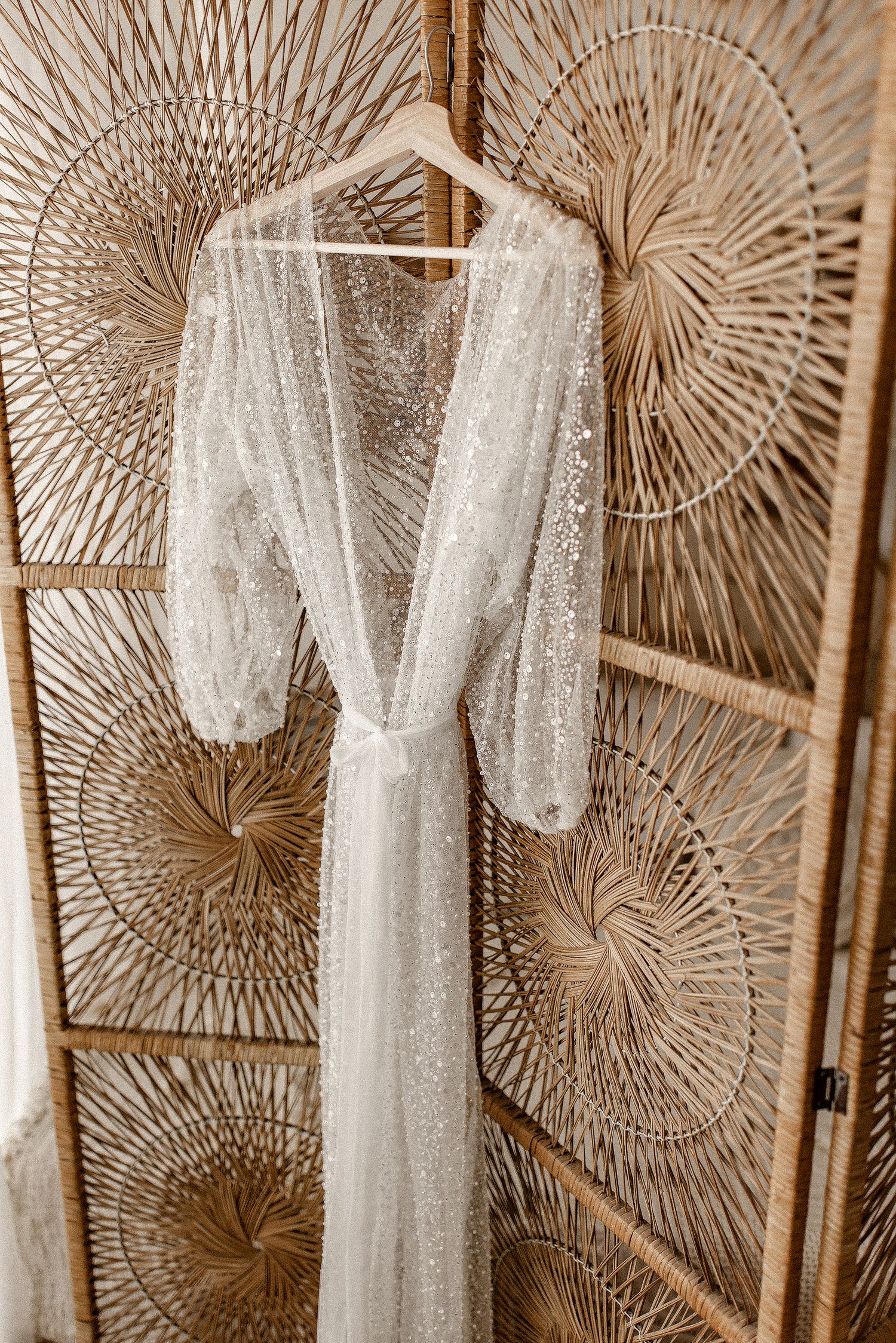 Elegant white lace wedding dress with long sleeves hanging against decorative fan-shaped wall decor.