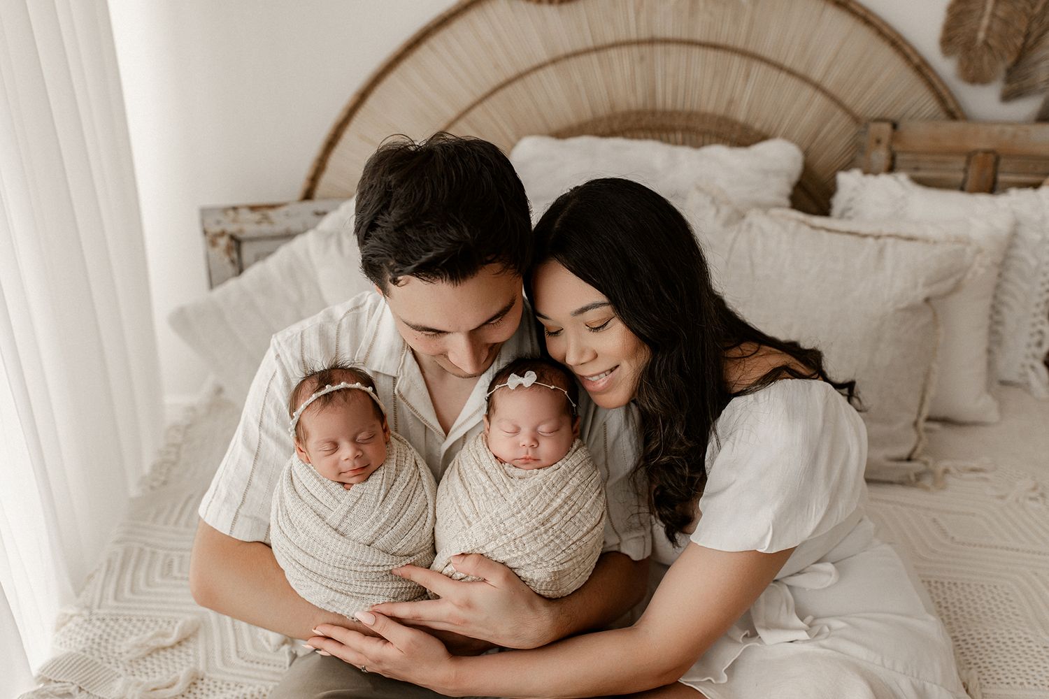 A series of intimate black and white family photos showing tender moments between parents and baby on a white bed.