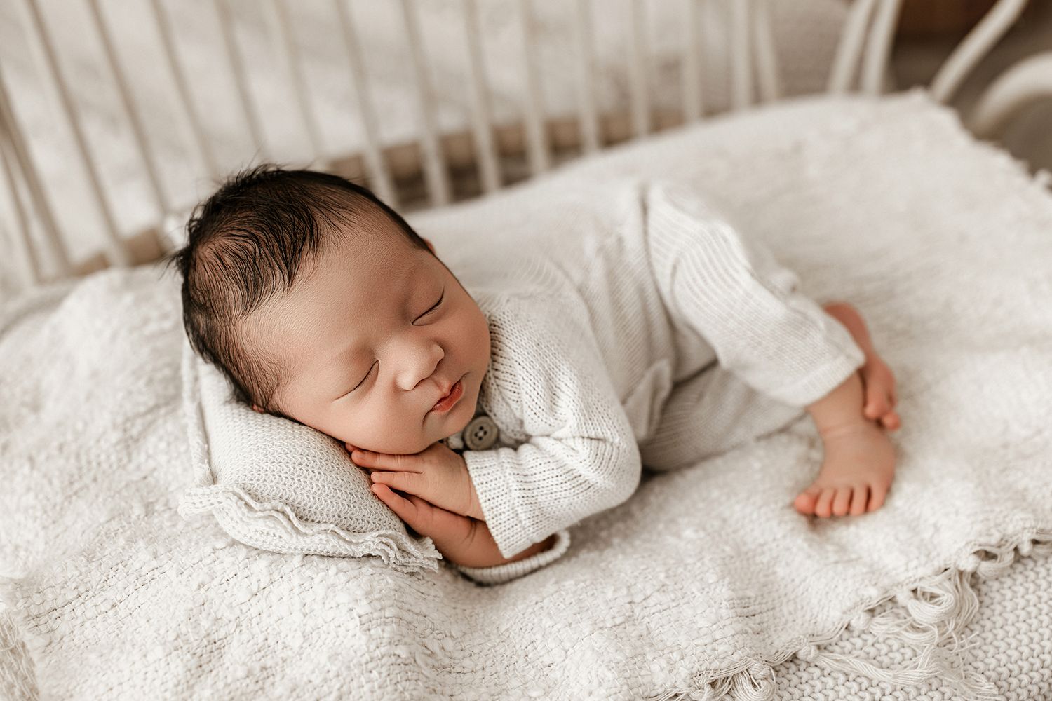 A sleeping newborn baby lies peacefully on white lace bedding in a gentle studio setting.