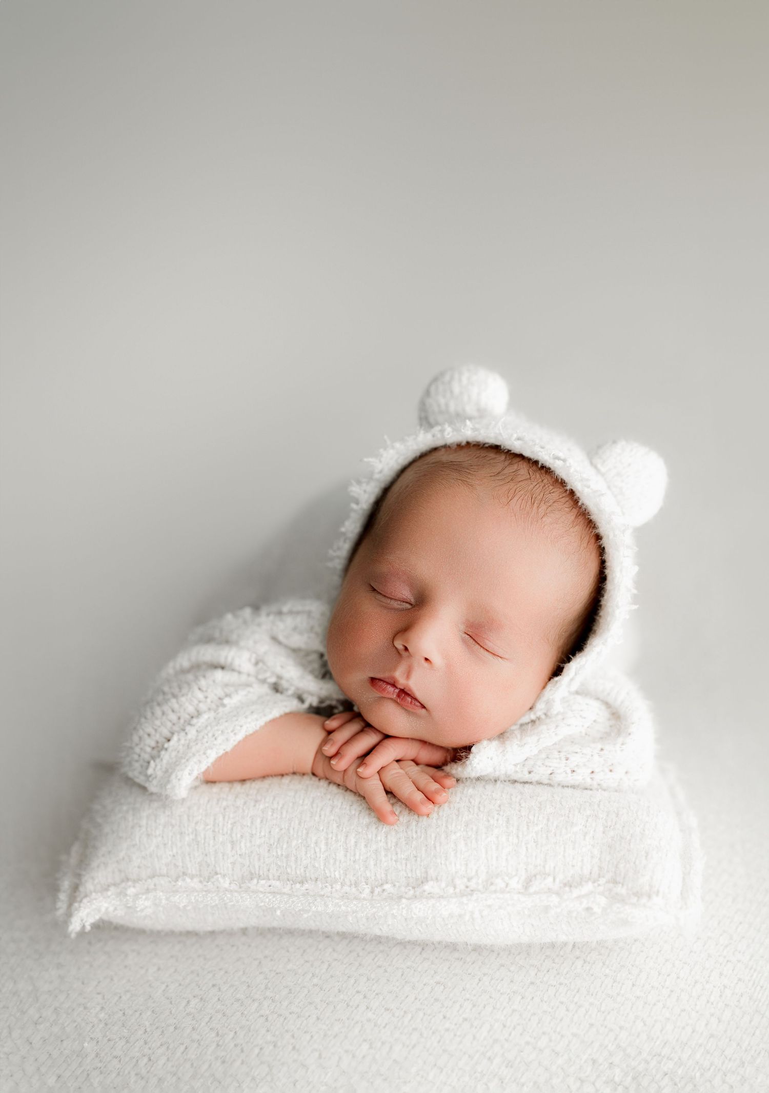 A sleeping newborn swaddled in soft white fabric lies peacefully on a light gray background.