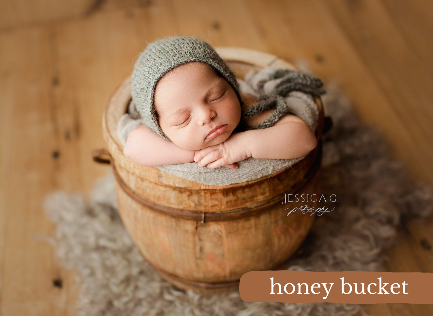 A sleeping newborn baby dressed in a gray bonnet rests peacefully in a vintage wooden honey bucket.