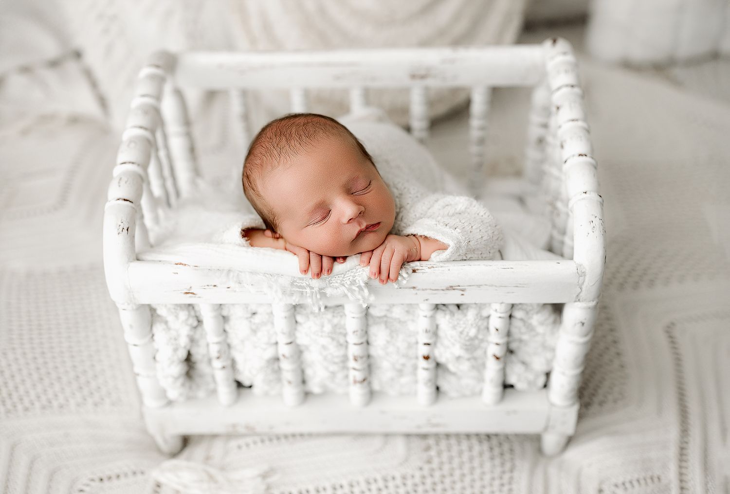 A sleeping newborn rests peacefully in a white vintage-style crib with ornate detailing.
