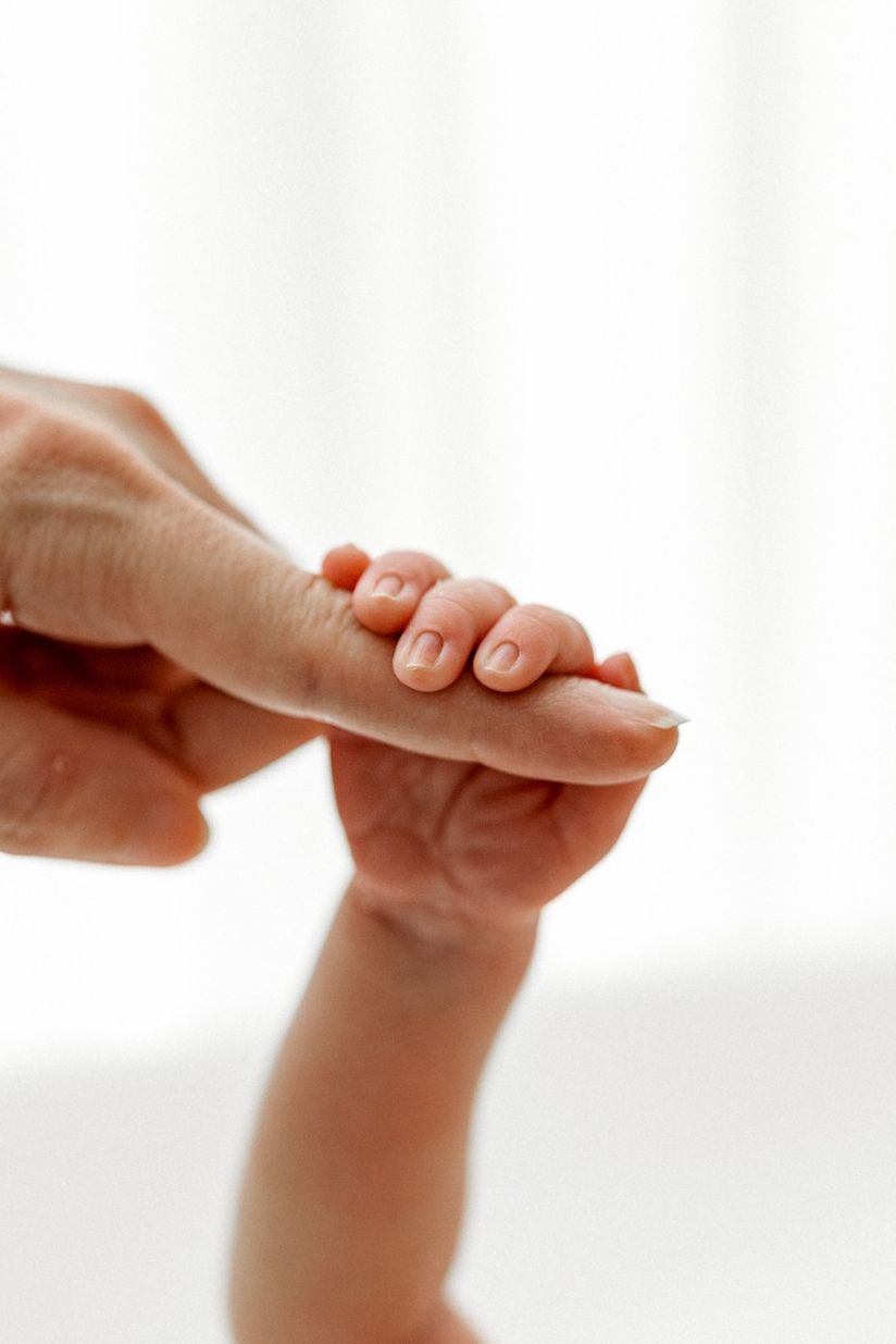 Close-up of a tiny newborn baby hand being gently held by adult fingers against a white background.