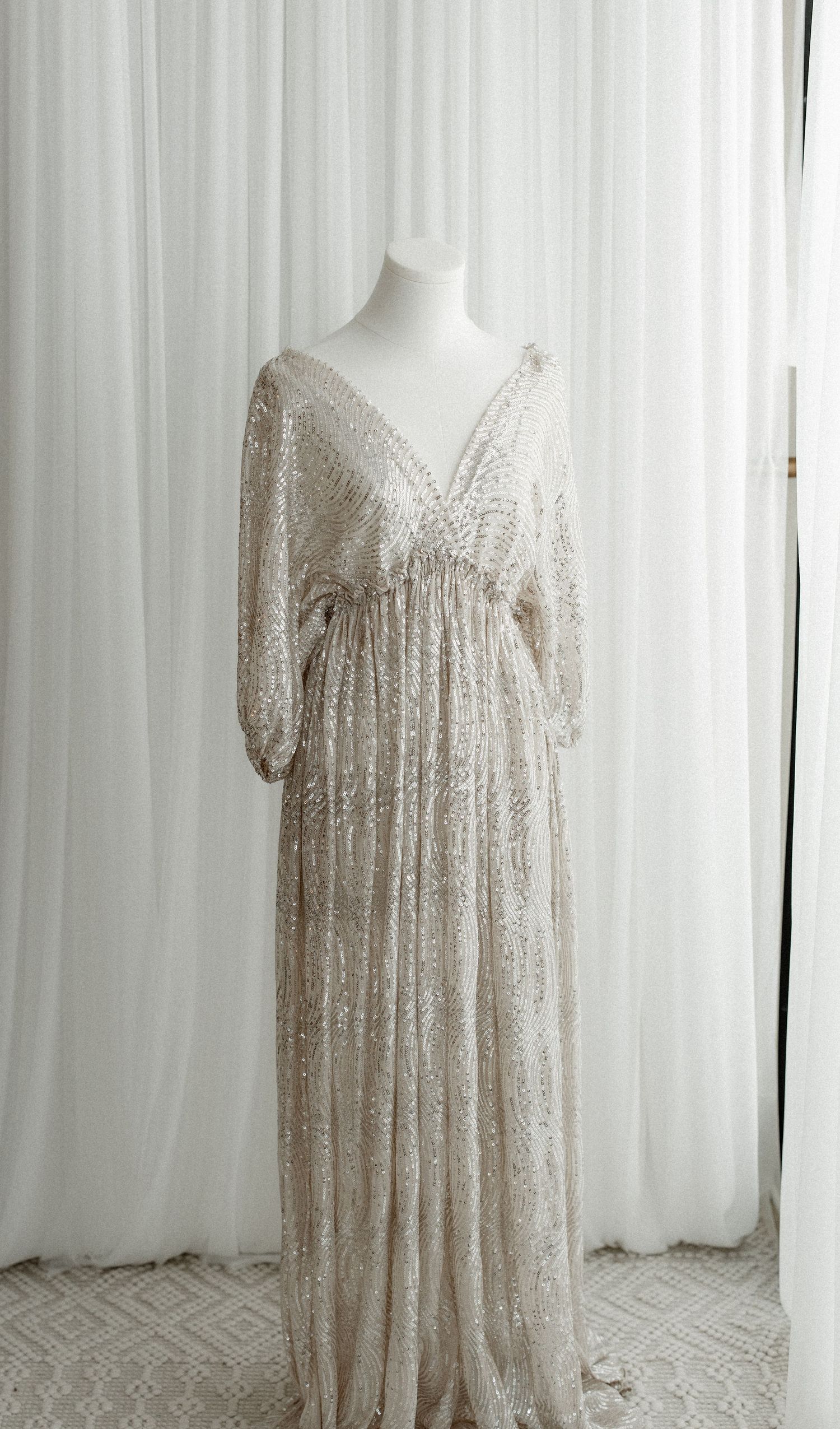 A delicate cream-colored lace dress with short sleeves displayed on a mannequin against a white curtain backdrop.