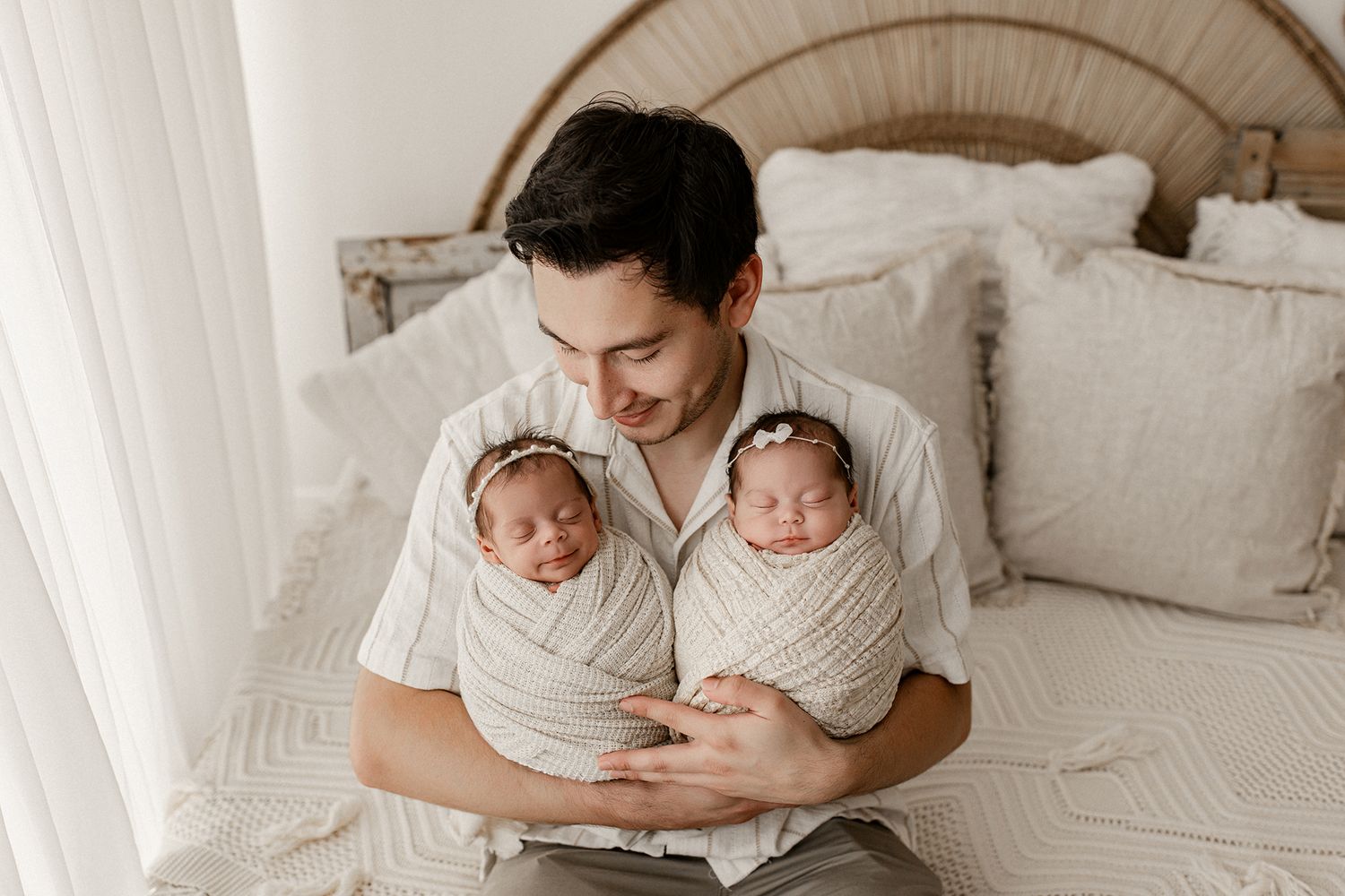 Intimate newborn photography session on white bed with parents cuddling their sleeping baby in natural light.