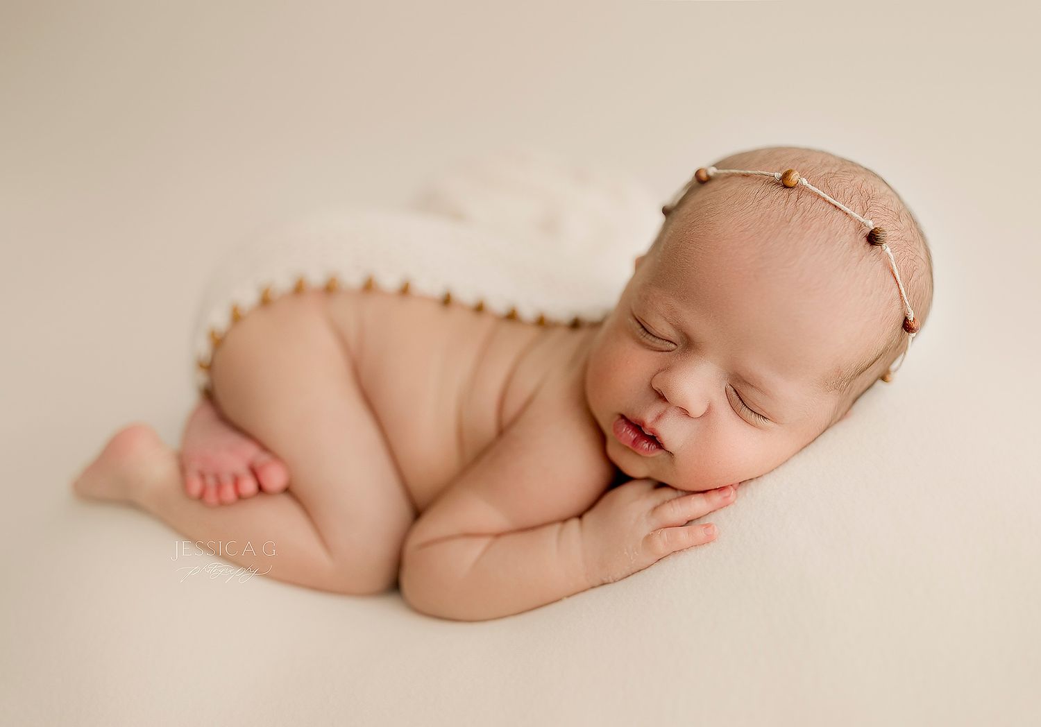 A sleeping newborn baby curled up peacefully on a cream-colored backdrop during a professional photo session.