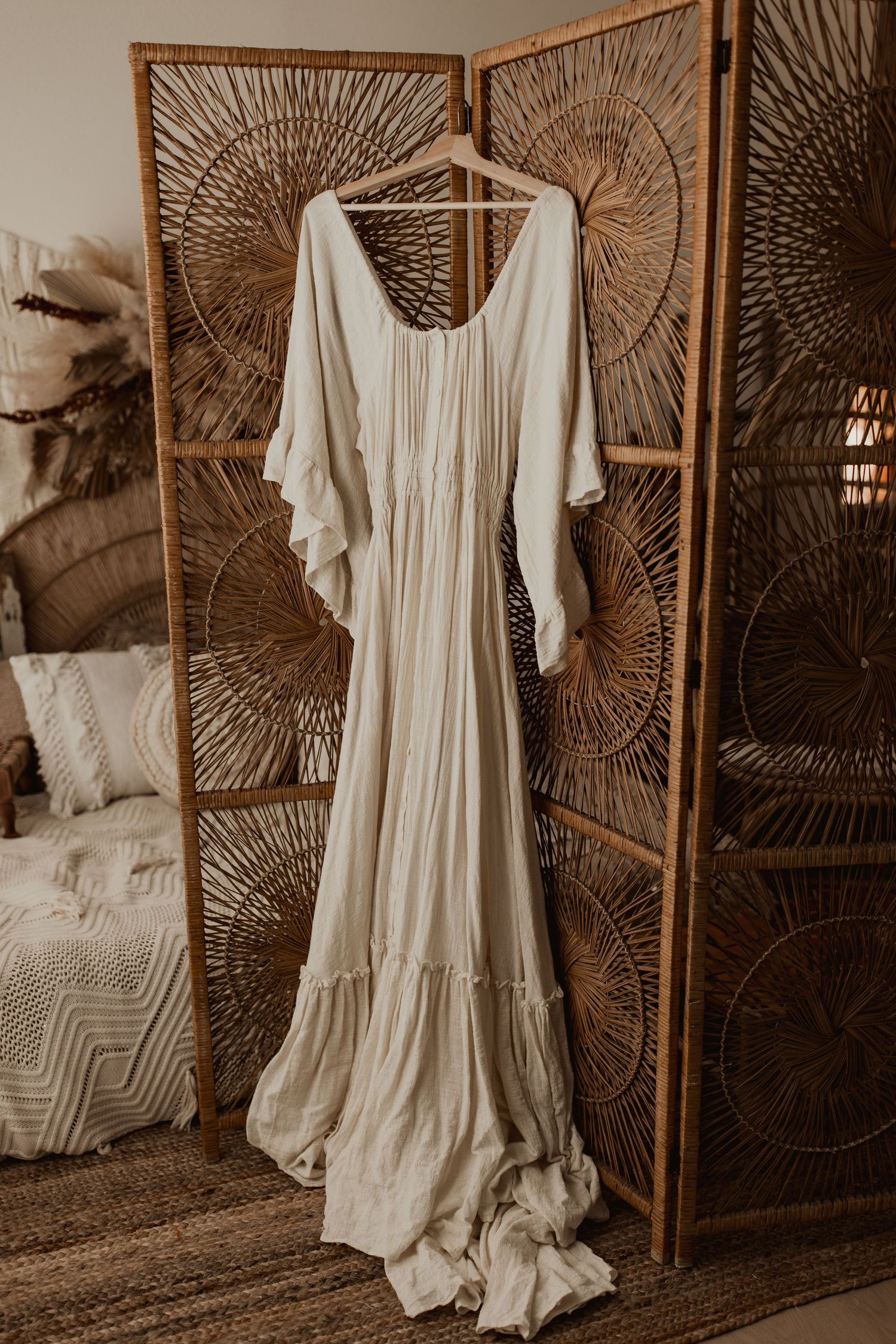 Flowing white maxi dress with flutter sleeves hanging on wooden folding screen.