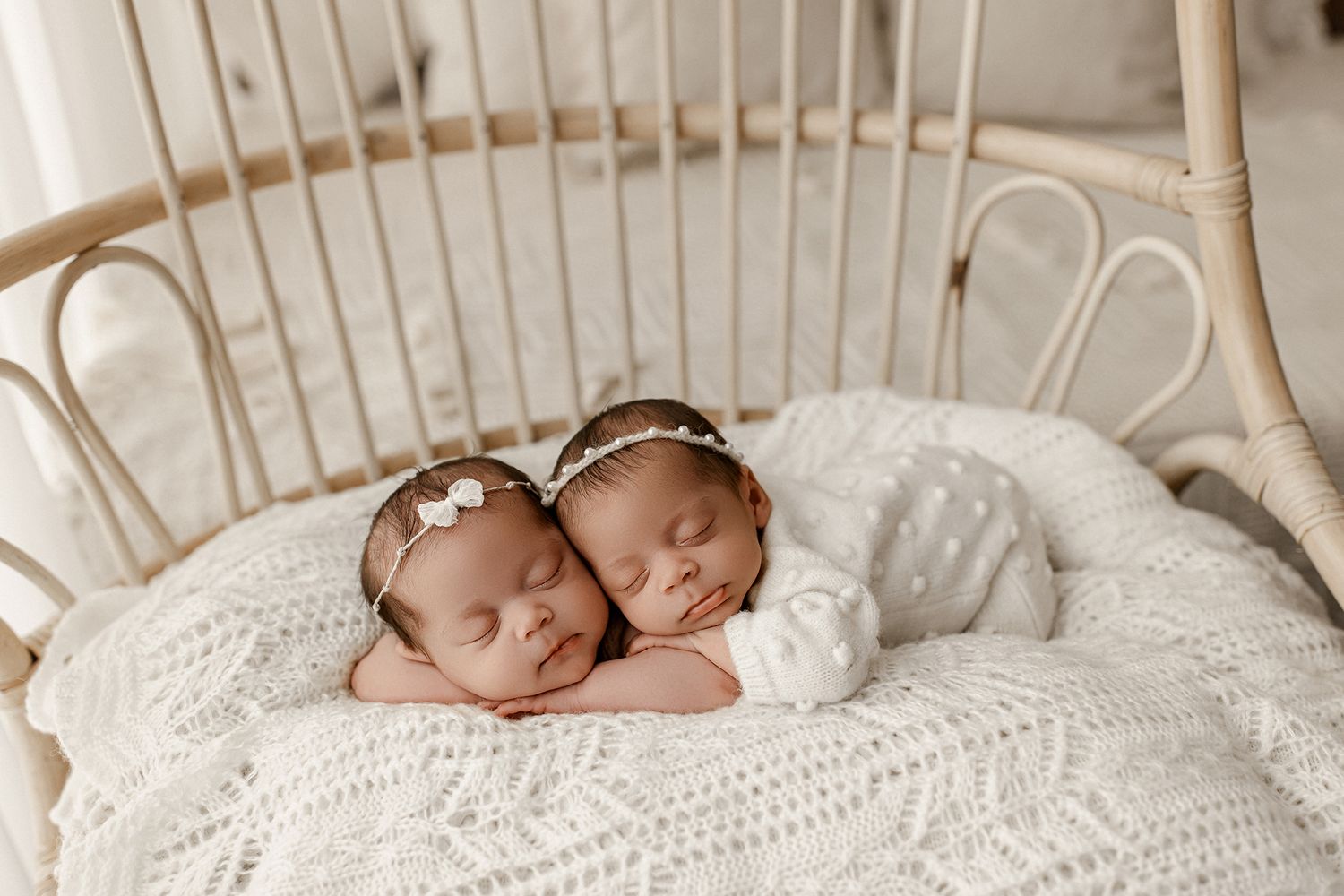 Sleeping newborn baby wrapped in white knit blanket lying on textured white fabric background.