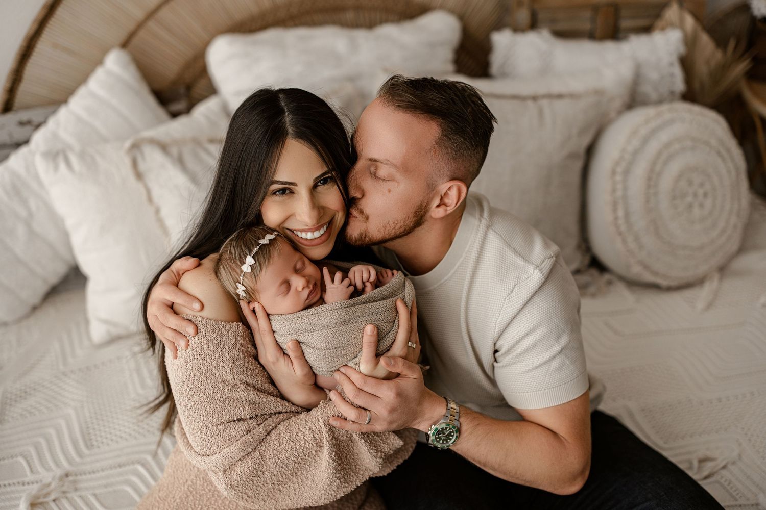 A couple shares an intimate moment sitting together in a bedroom with white pillows and cozy decor.
