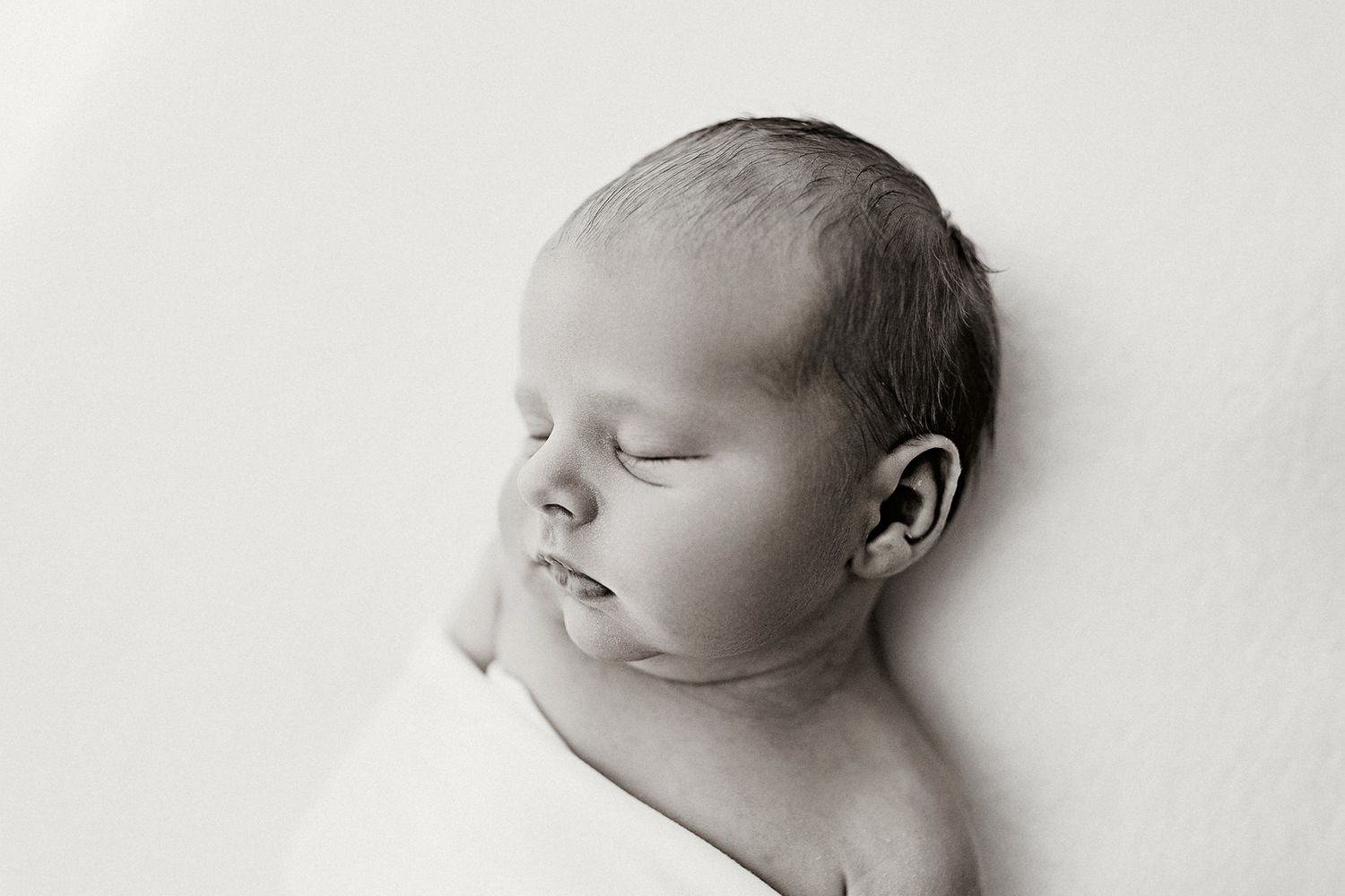 A peaceful sleeping newborn baby in black and white photography with soft lighting and gentle shadows.