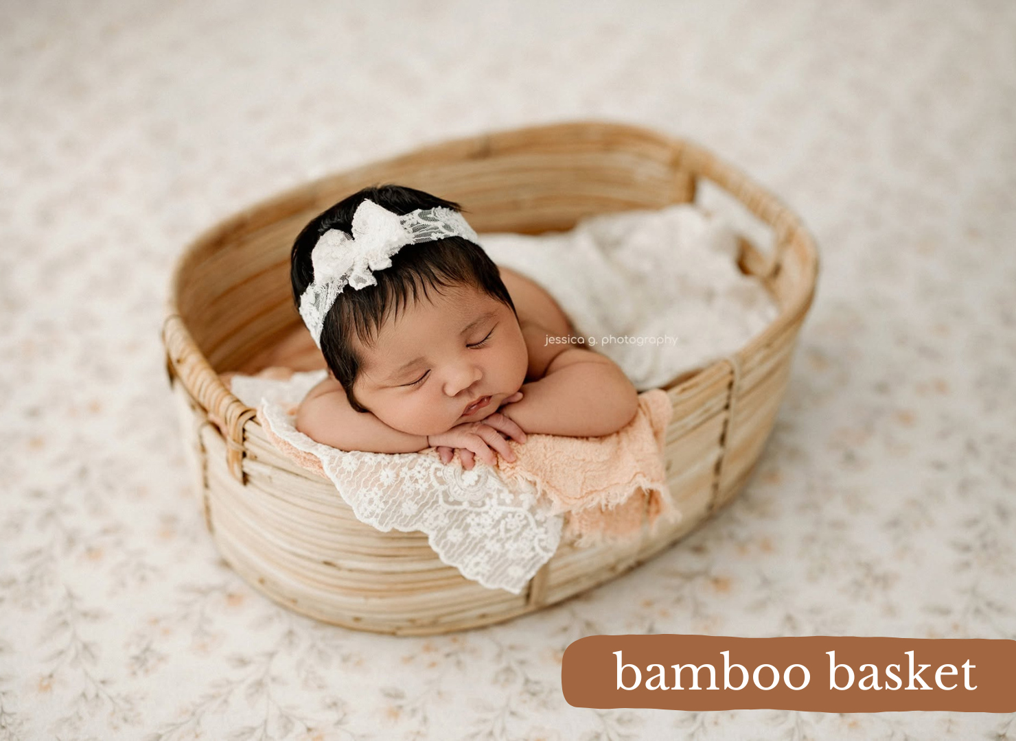 Newborn baby sleeping peacefully in a bamboo basket with lace fabric and a white bow headband.