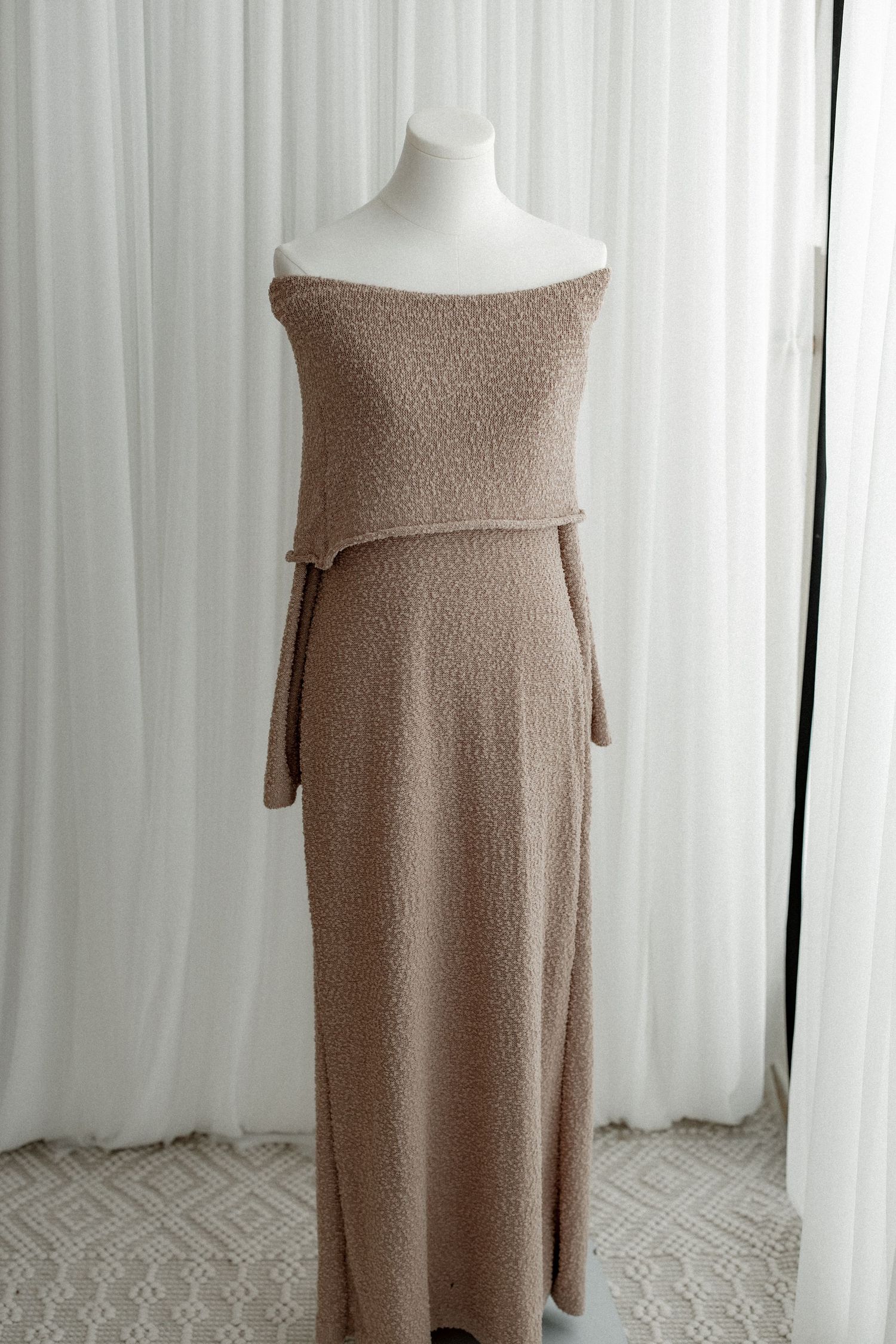 Elegant off-shoulder beige knit maxi dress with long sleeves displayed on white mannequin against light curtain background.
