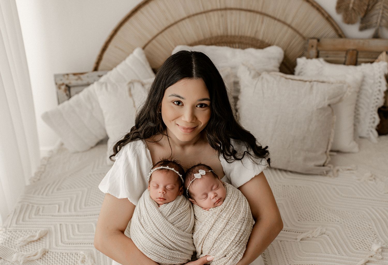 A series of five tender black and white photos showing a parent with newborn twins in a cozy bedroom setting.
