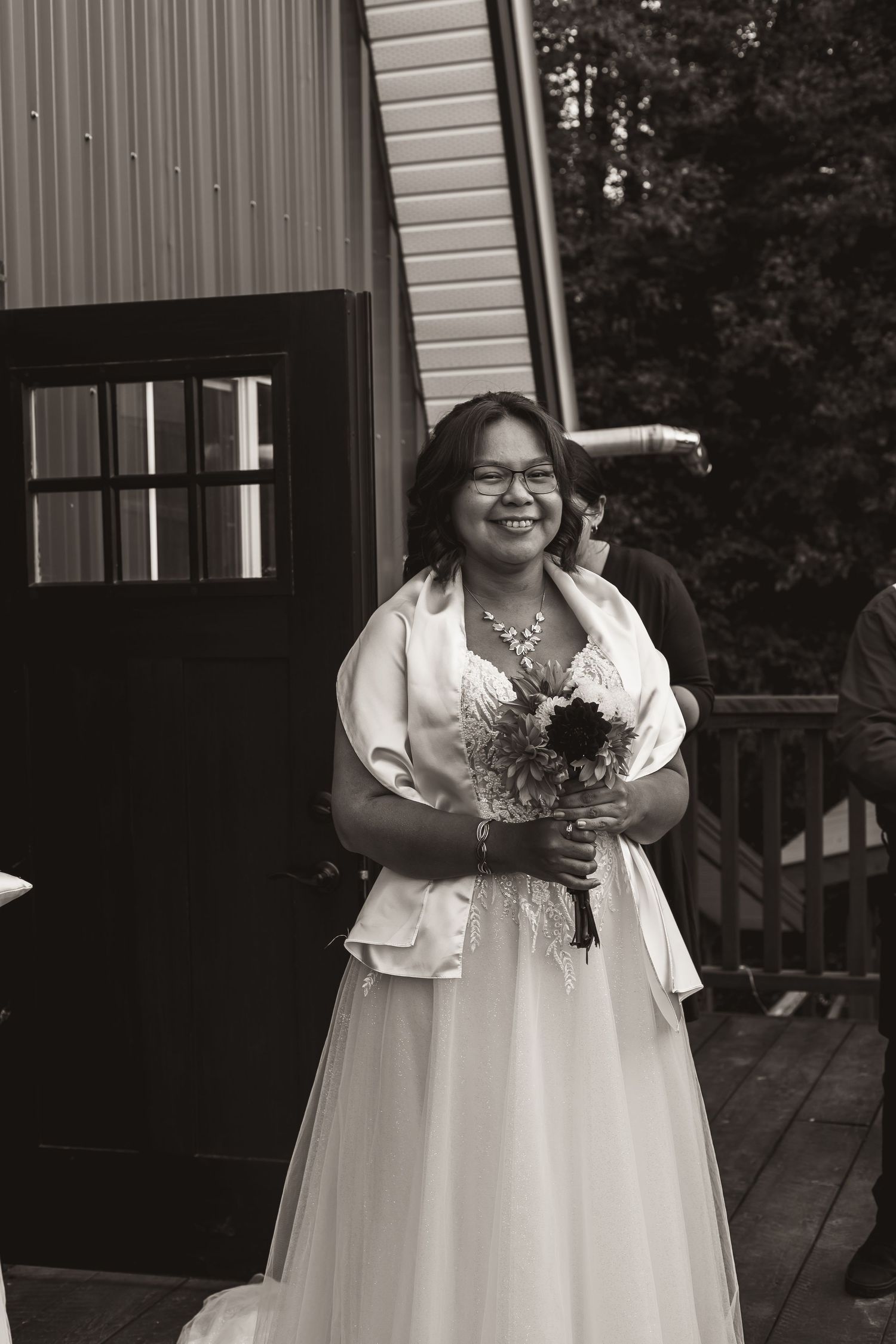 A joyful moment captured in black and white as someone holds a wedding bouquet on a wooden deck.