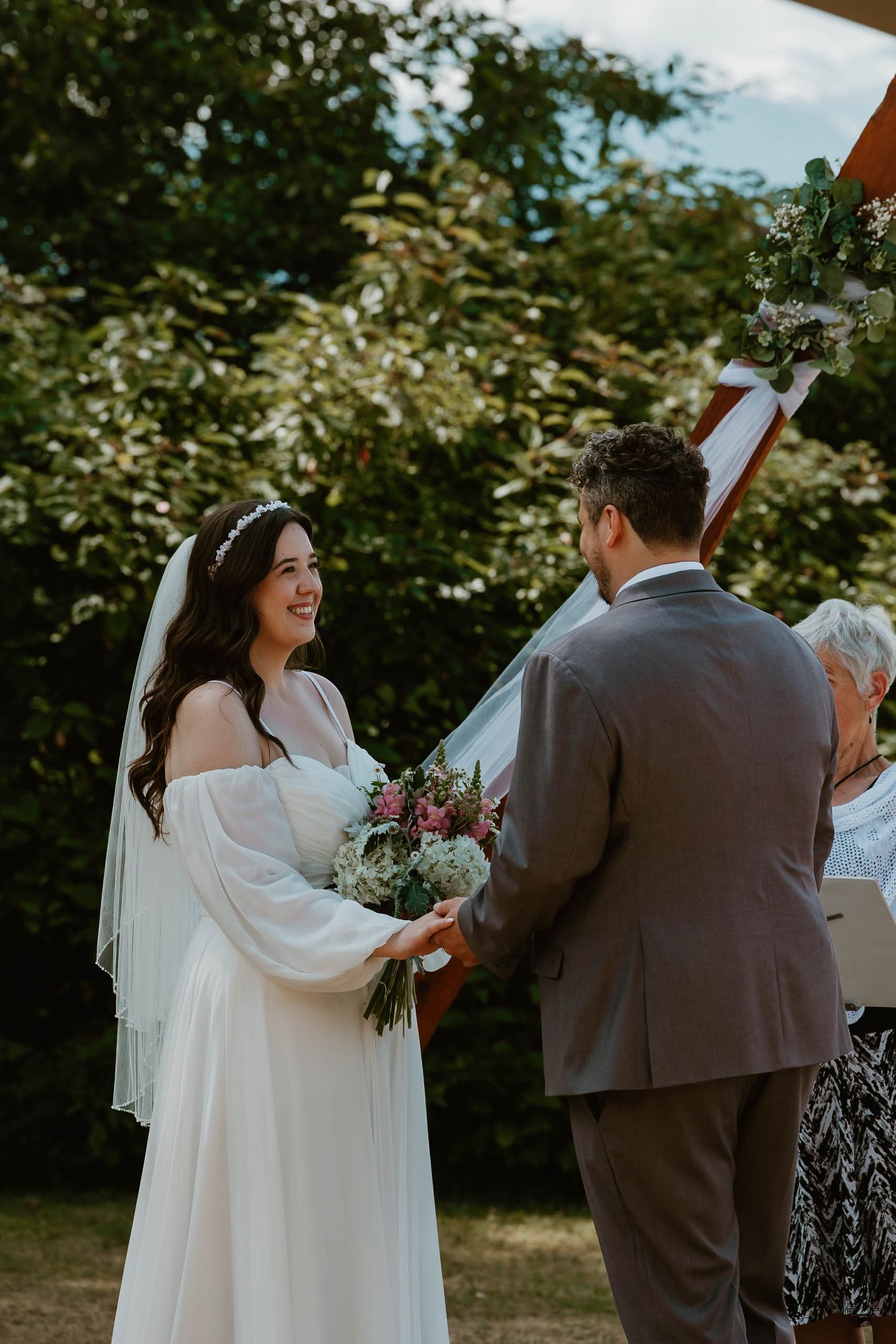 A couple shares a joyful moment during their outdoor wedding ceremony under wooden arch decor.