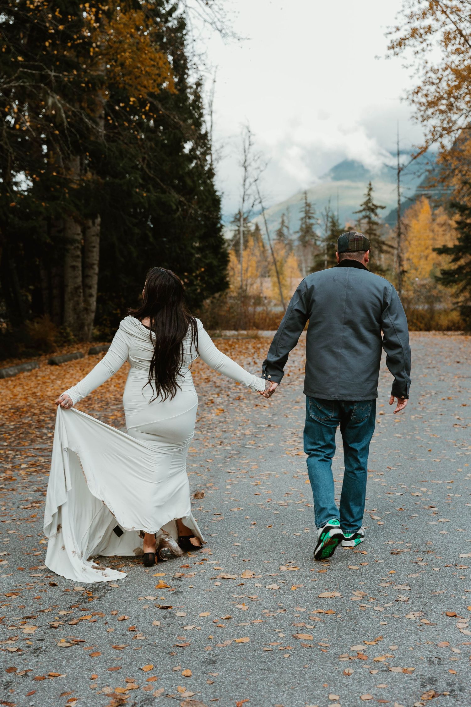 A couple walks along a leaf-covered path during fall with mountains in the background.