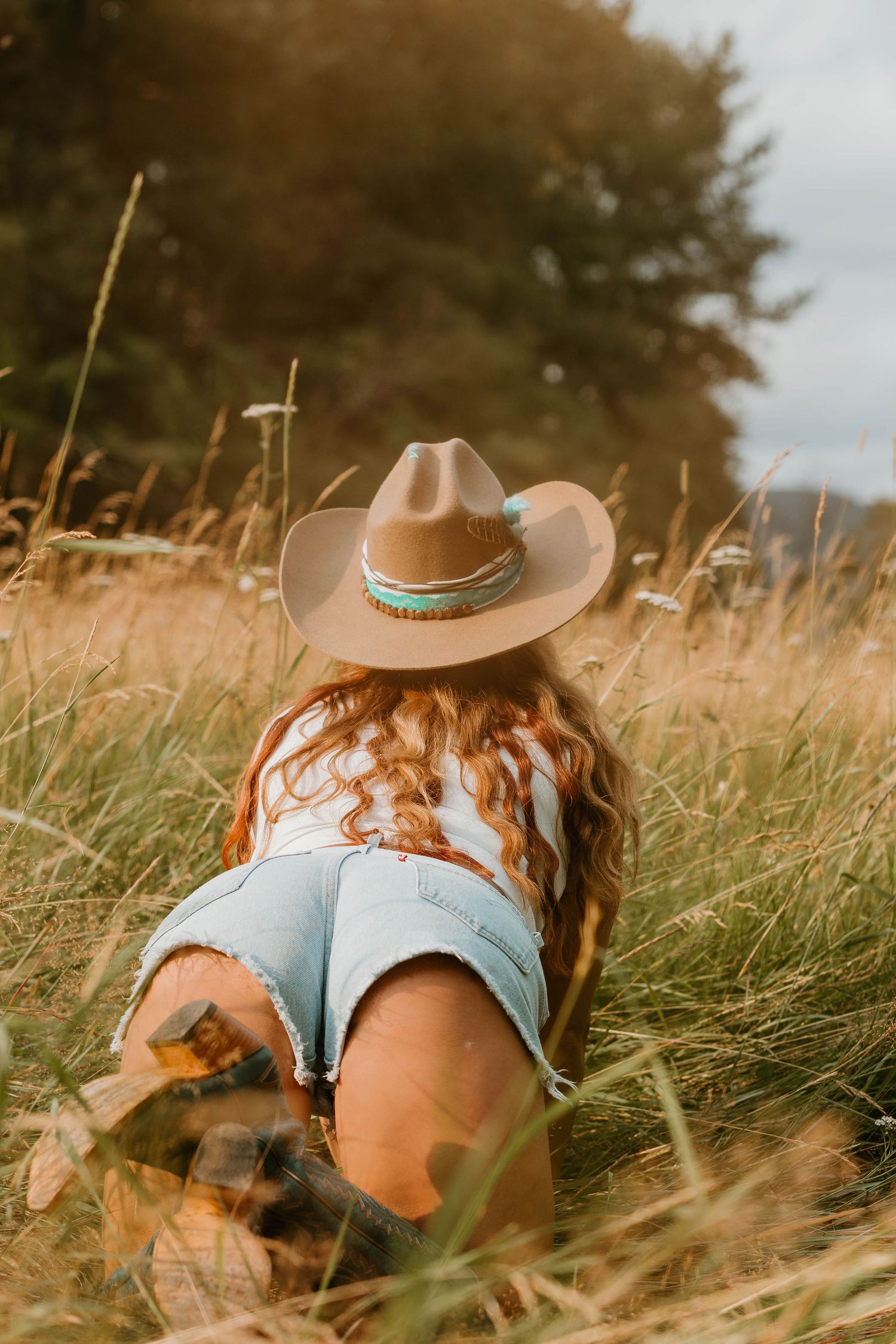 Cowboy hat and denim shorts in golden wheat field during sunset.