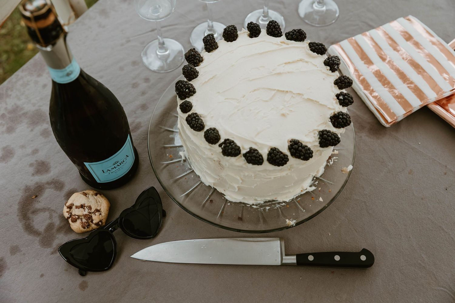 A white frosted cake decorated with dark chocolate oreos around the top edge sits beside a wine bottle and knife.