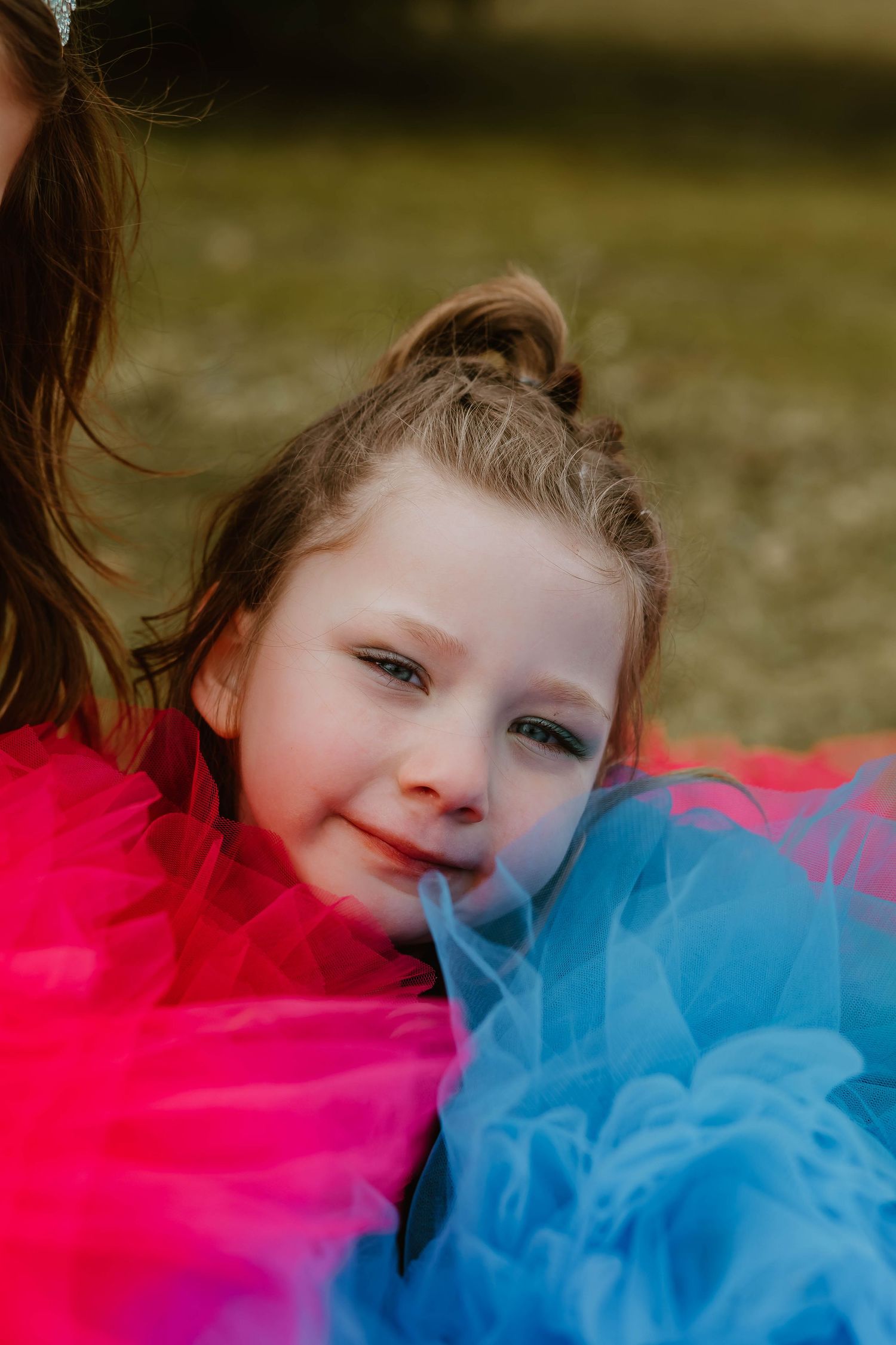A bright, colorful portrait with tulle fabric in vibrant red and blue creating a whimsical backdrop.