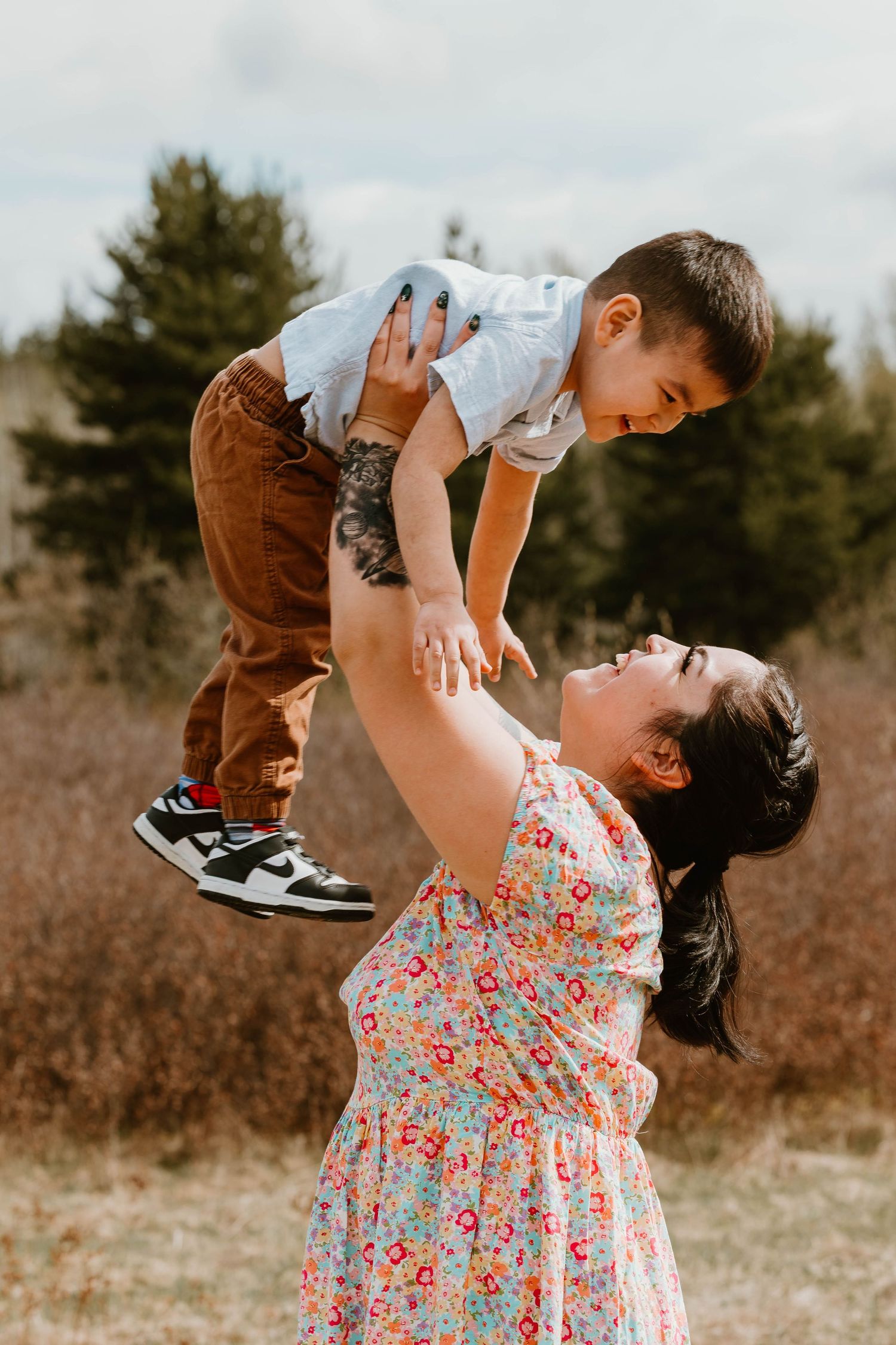 Playful moment captured as parent lifts child in floral dress against nature backdrop.