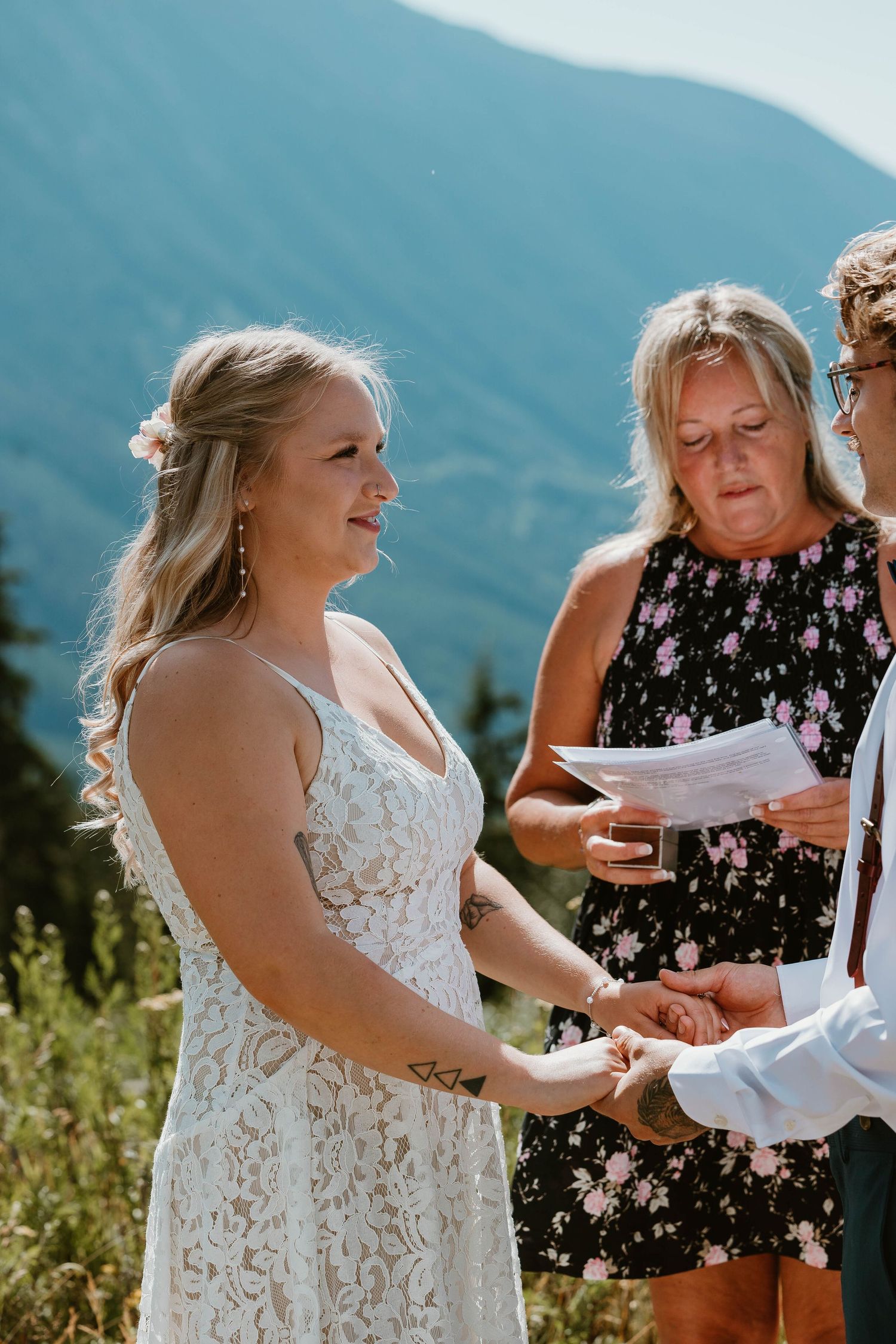 An outdoor wedding ceremony with attendees standing on a blanket against mountain vistas.