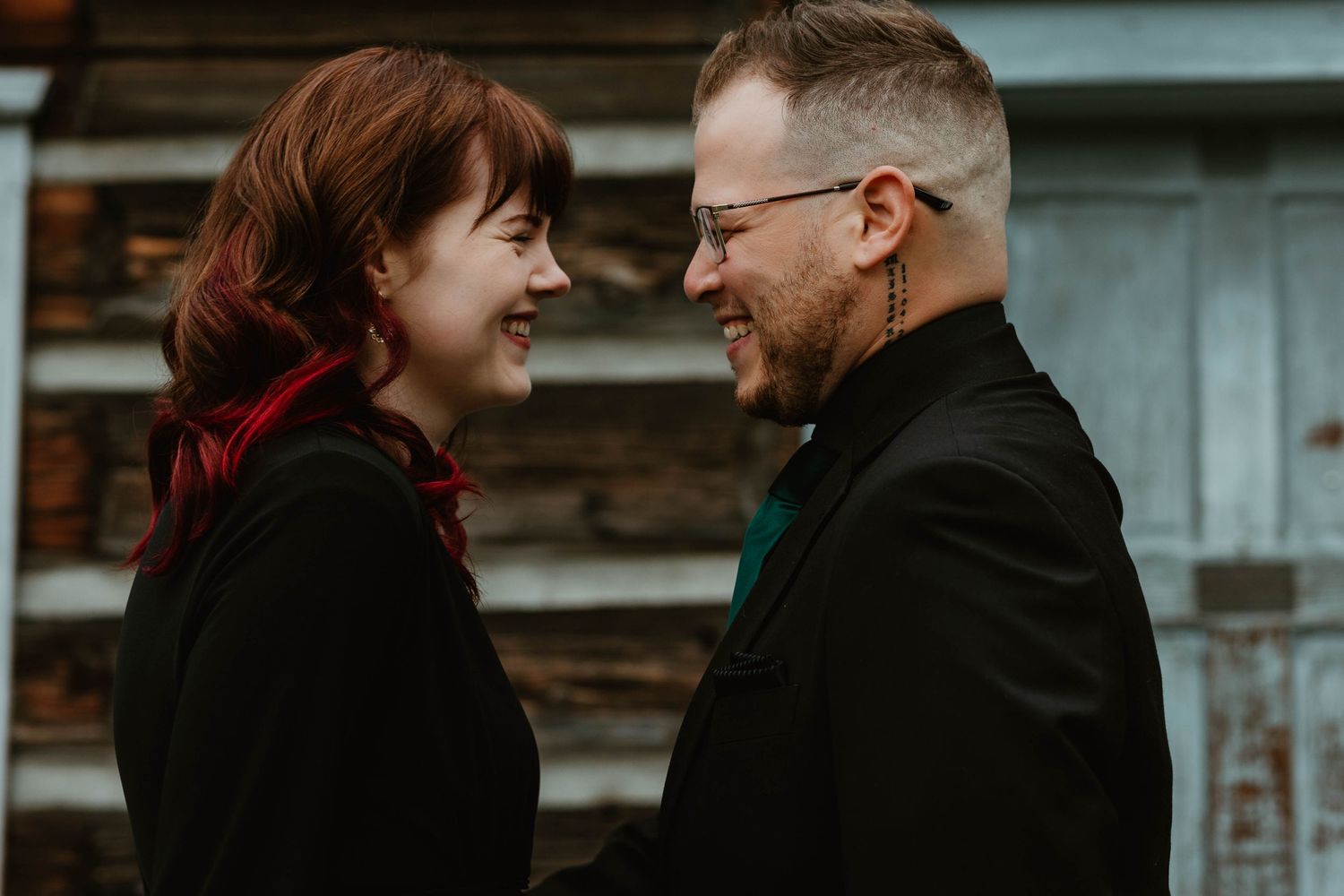 A joyful moment shared between a couple against a rustic wooden wall.