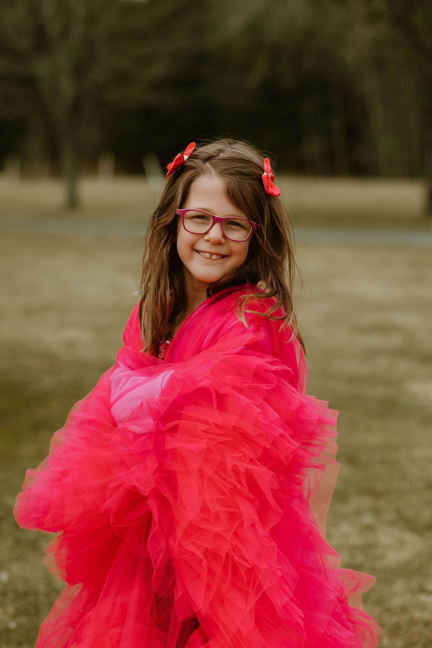 A bright pink tulle dress twirls against a natural outdoor background on a winter day.
