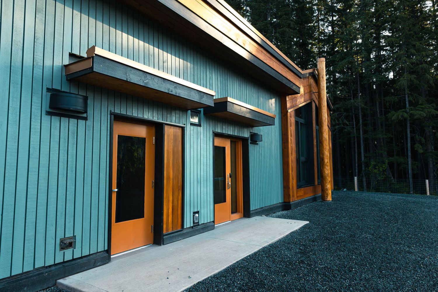 Commercial building entrance with teal siding and wooden trim accents against forest backdrop.