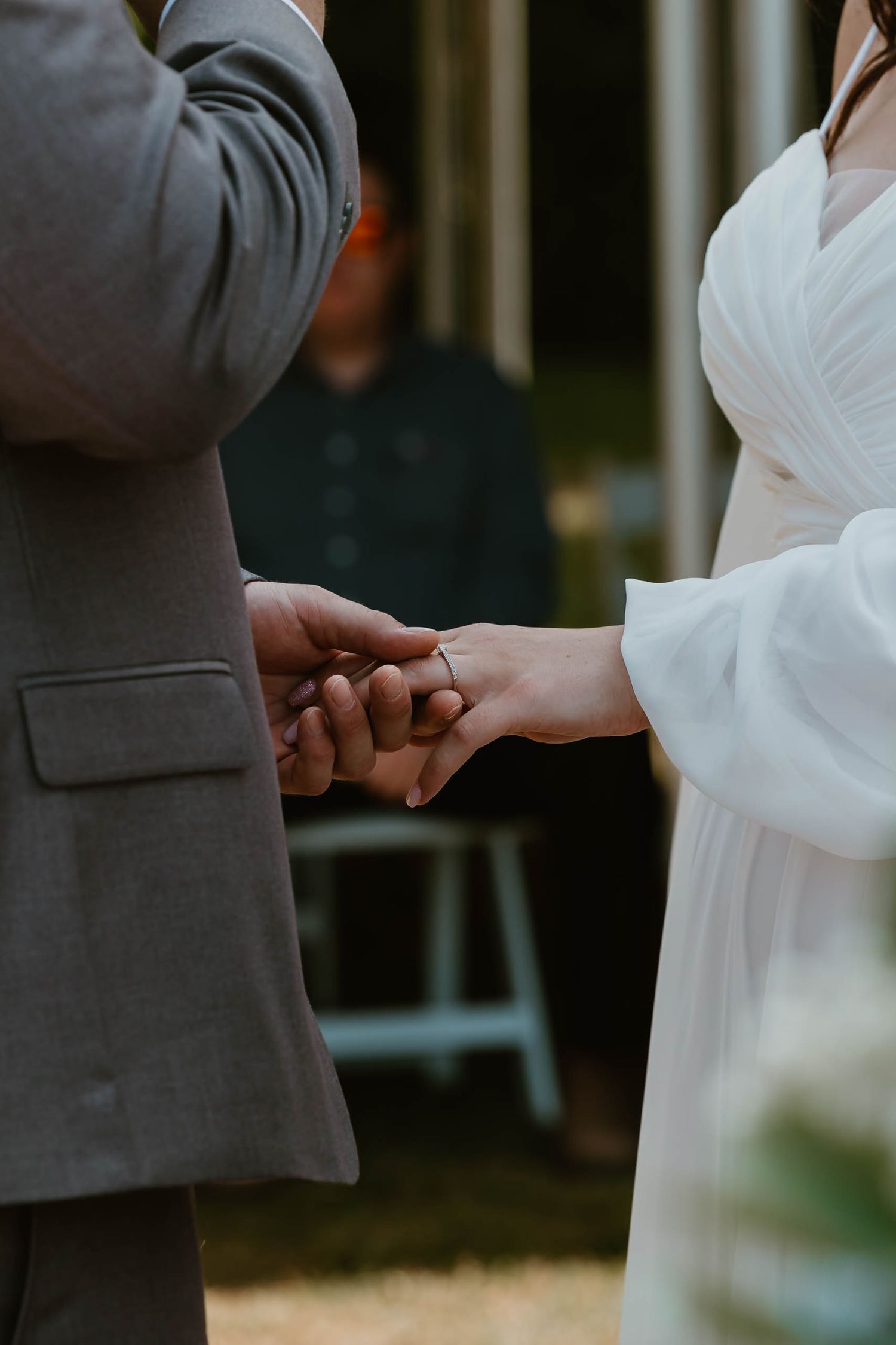 Close-up of hands exchanging rings during an outdoor wedding ceremony.