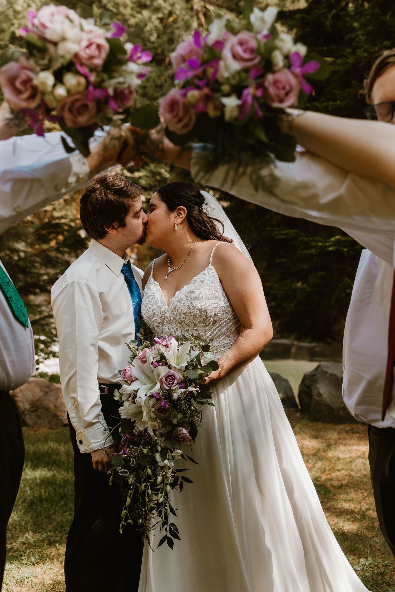 Wedding couple shares romantic kiss under floral arch in outdoor garden setting.