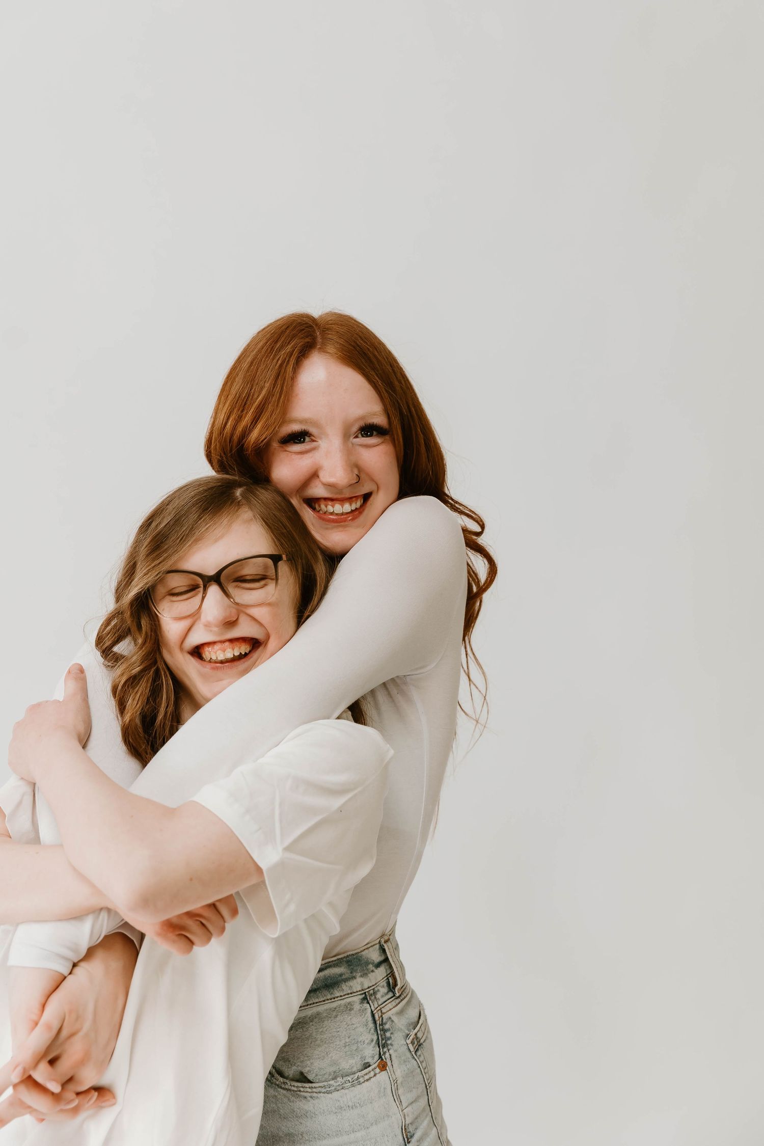 Two friends sharing a joyful embrace and laughing together against a white background.
