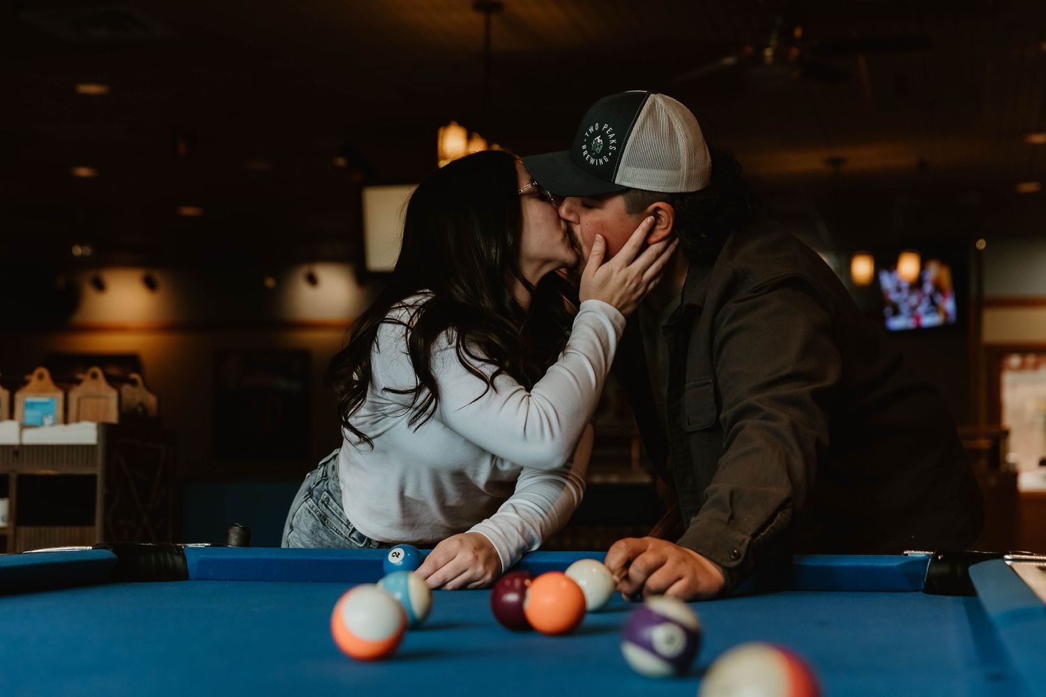 Romantic couple shares an intimate moment while playing pool at a dimly lit bar.