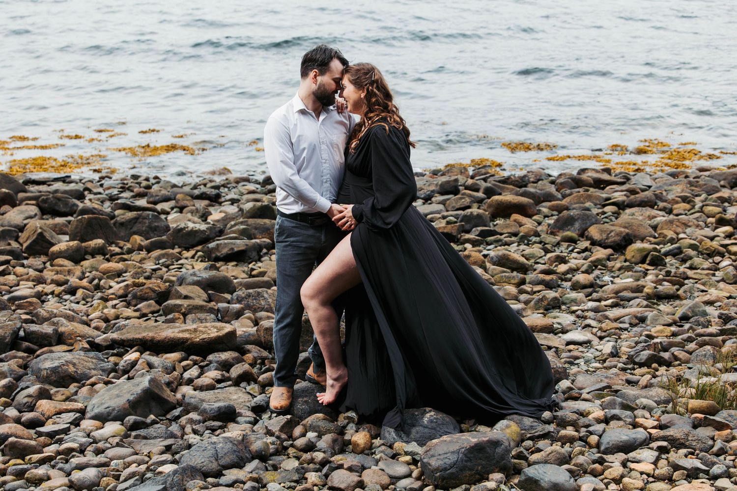A romantic moment on rocky coastal shores with flowing black dress and dramatic landscape.