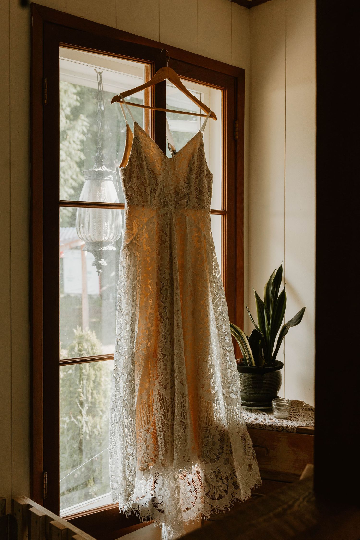Elegant lace wedding dress hanging in window with natural light streaming through.