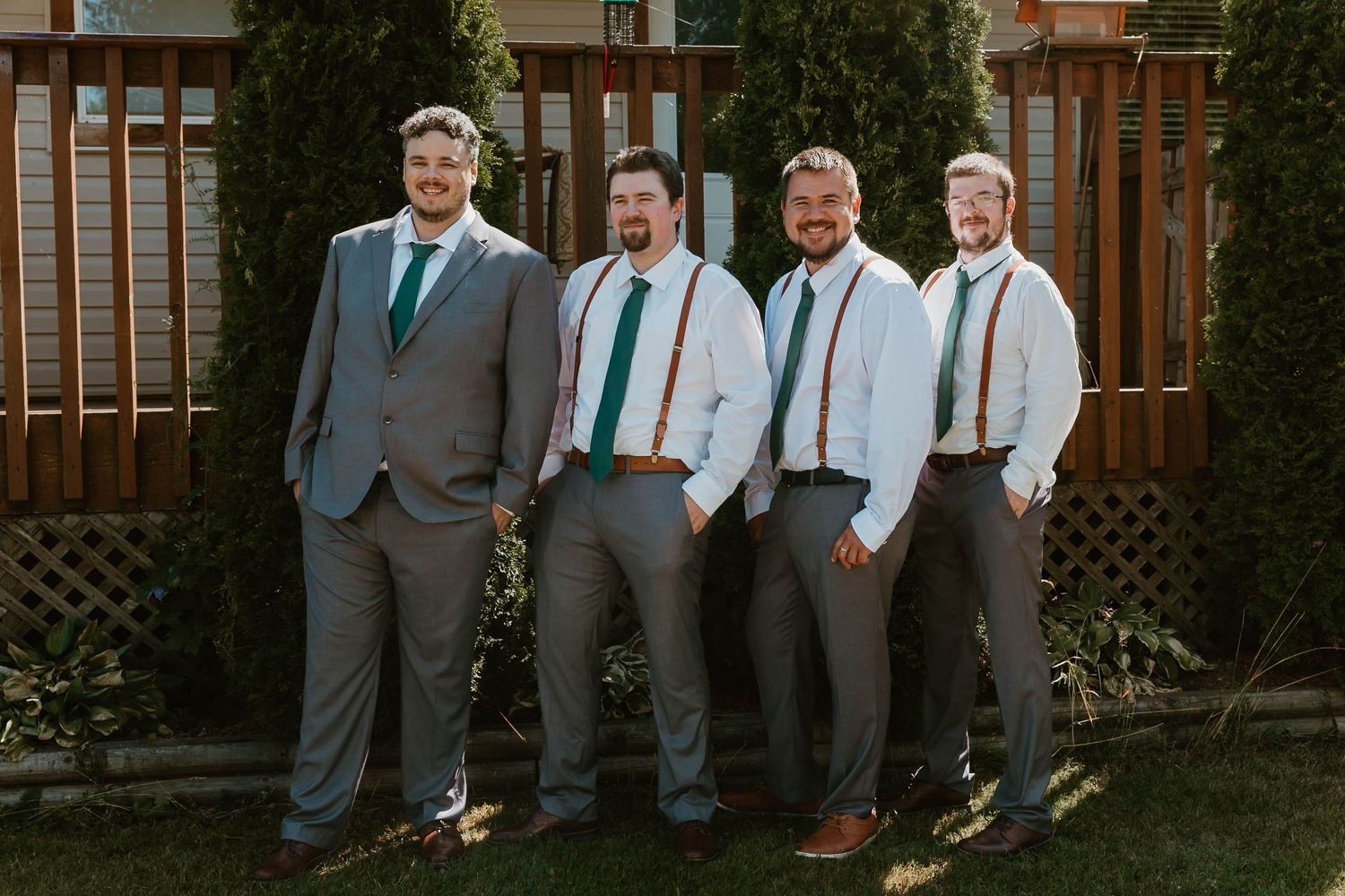 Groomsmen in coordinated grey suits and teal ties pose together in backyard setting.