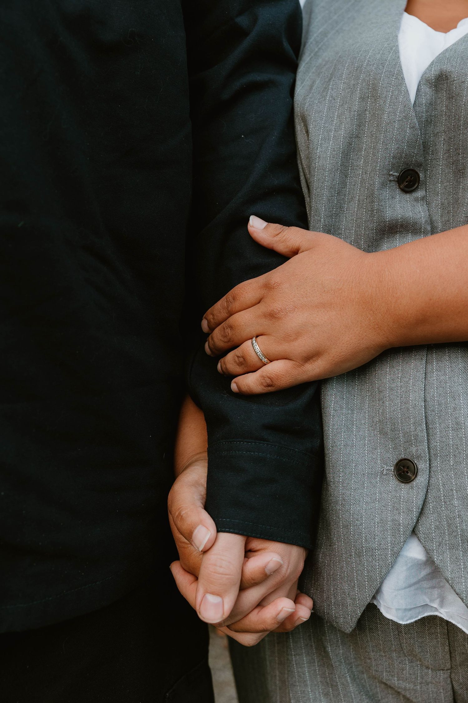 Close-up of clasped hands showing wedding rings and formal attire.