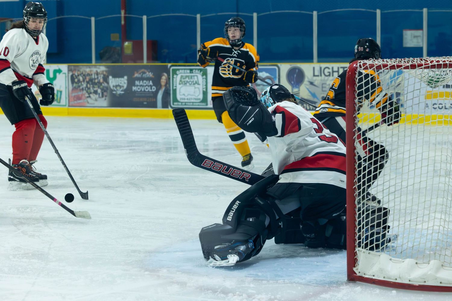 Hockey goalie makes save while players fight for puck near goal crease.