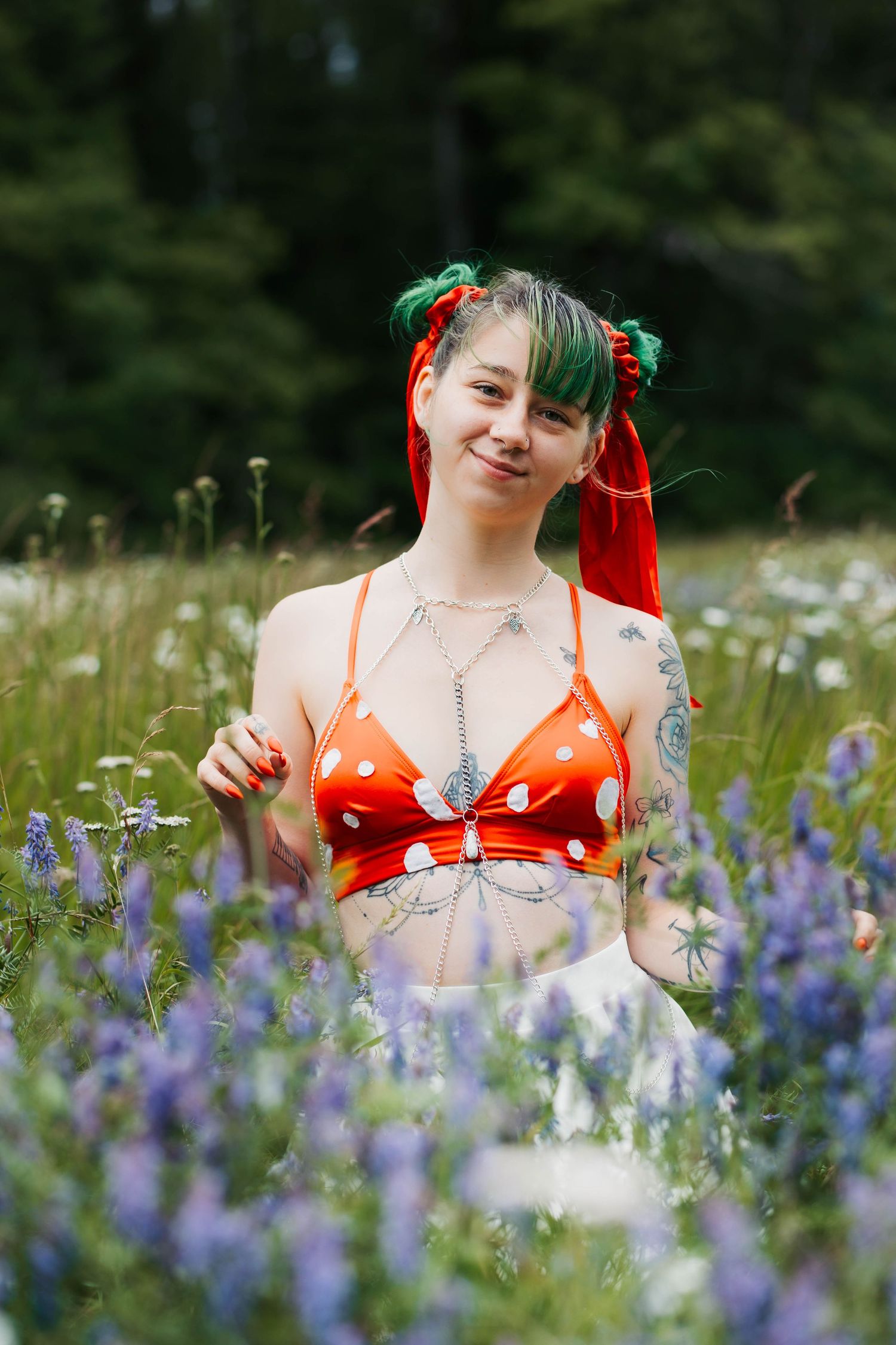 Alternative style portrait in orange polka dot top amid blooming wildflowers and greenery.